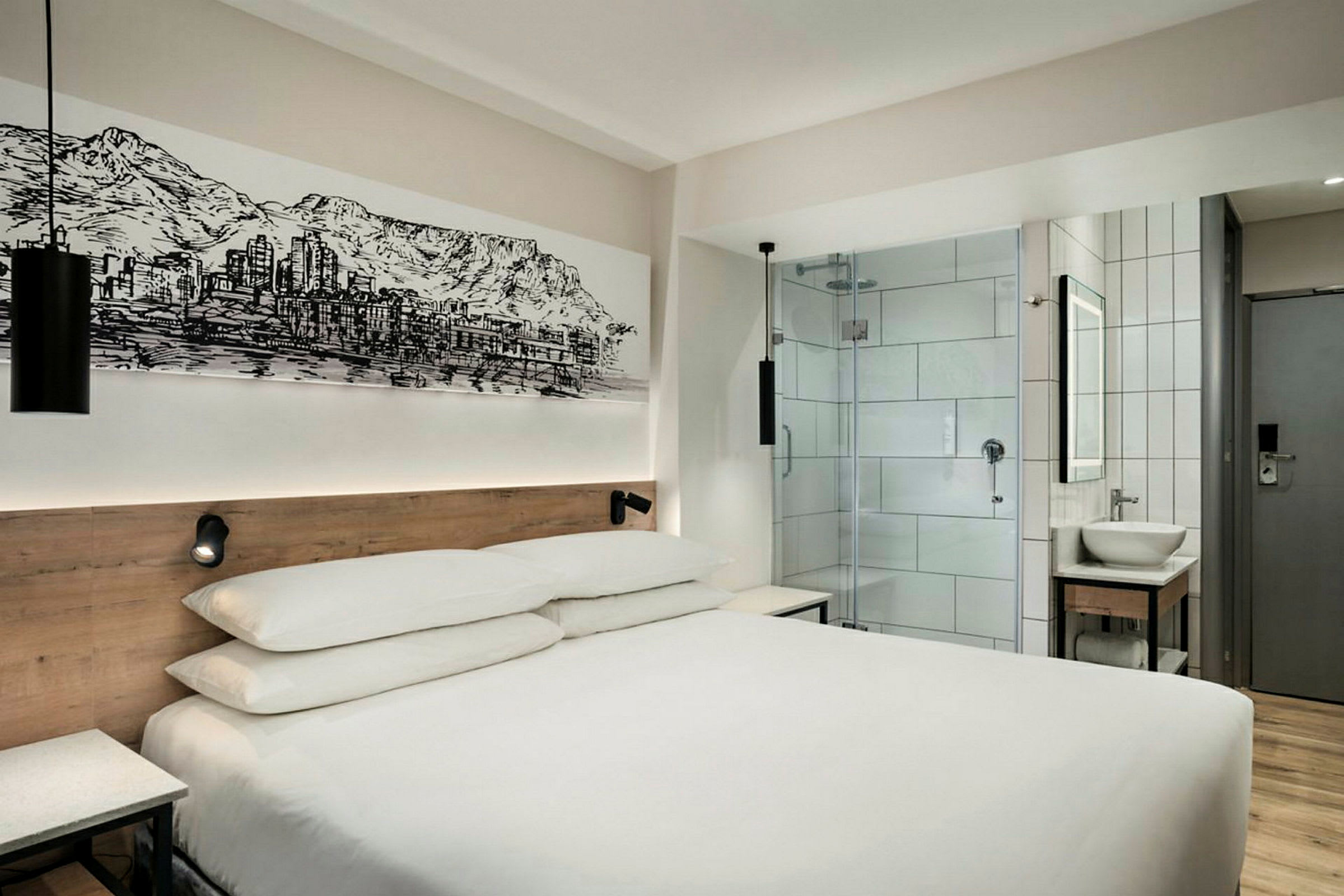 Moderni hotellihuone, jossa on parisänky, lasiovi kylpyhuoneeseen ja seinätaidetta. (Tekoälyn luoma teksti)
