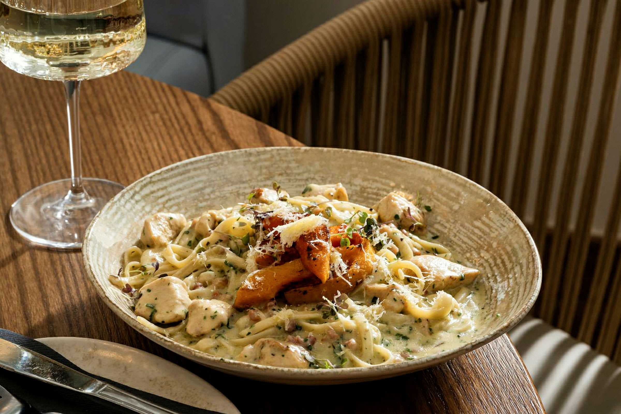 Lautanen pastaa kermakastikkeella ja lisukkeilla, tarjoiltuna ruokapöydällä valkoviinilasillisen kanssa. (Tekoälyn luoma teksti)