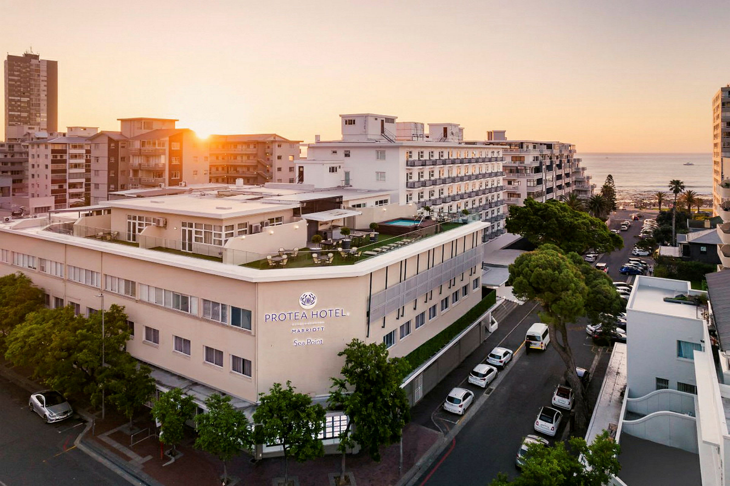 Hotellirakennus meren rannalla muiden rakennusten ympäröimänä auringonlaskussa. (Tekoälyn luoma teksti)