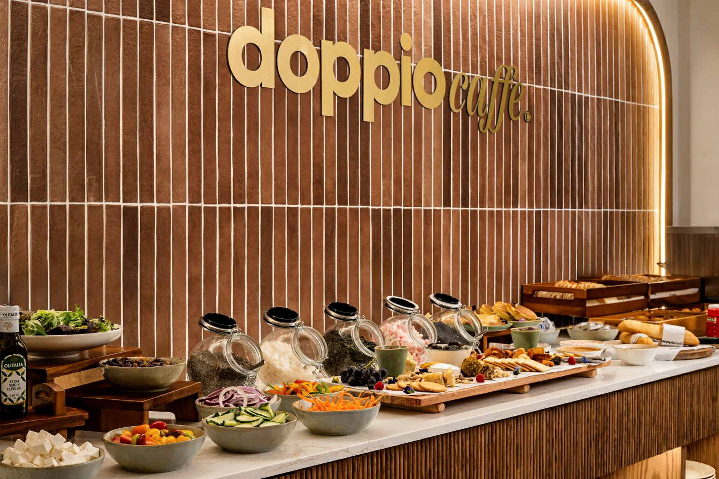 Kuva buffetista, jossa on erilaisia ruokia ja salaattiaineksia, seinän edessä, jossa lukee "Doppio Caffe". (Tekoälyn luoma teksti)