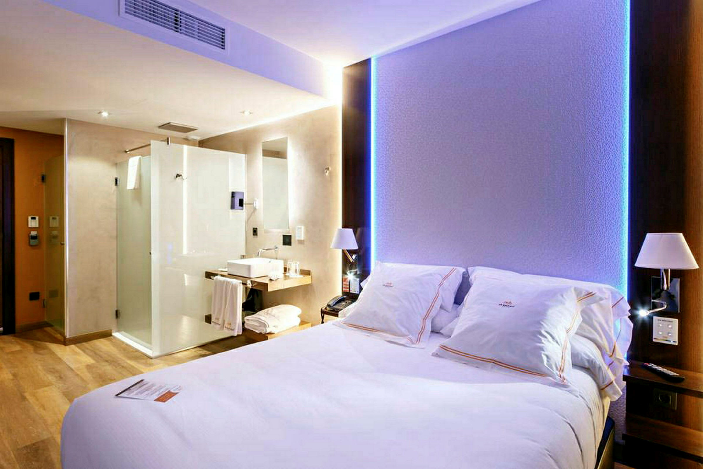 Hotellihuone, jossa on suuri sänky, valoisa sisustus ja näkyvät kylpyhuonetilat. (Tekoälyn luoma teksti)