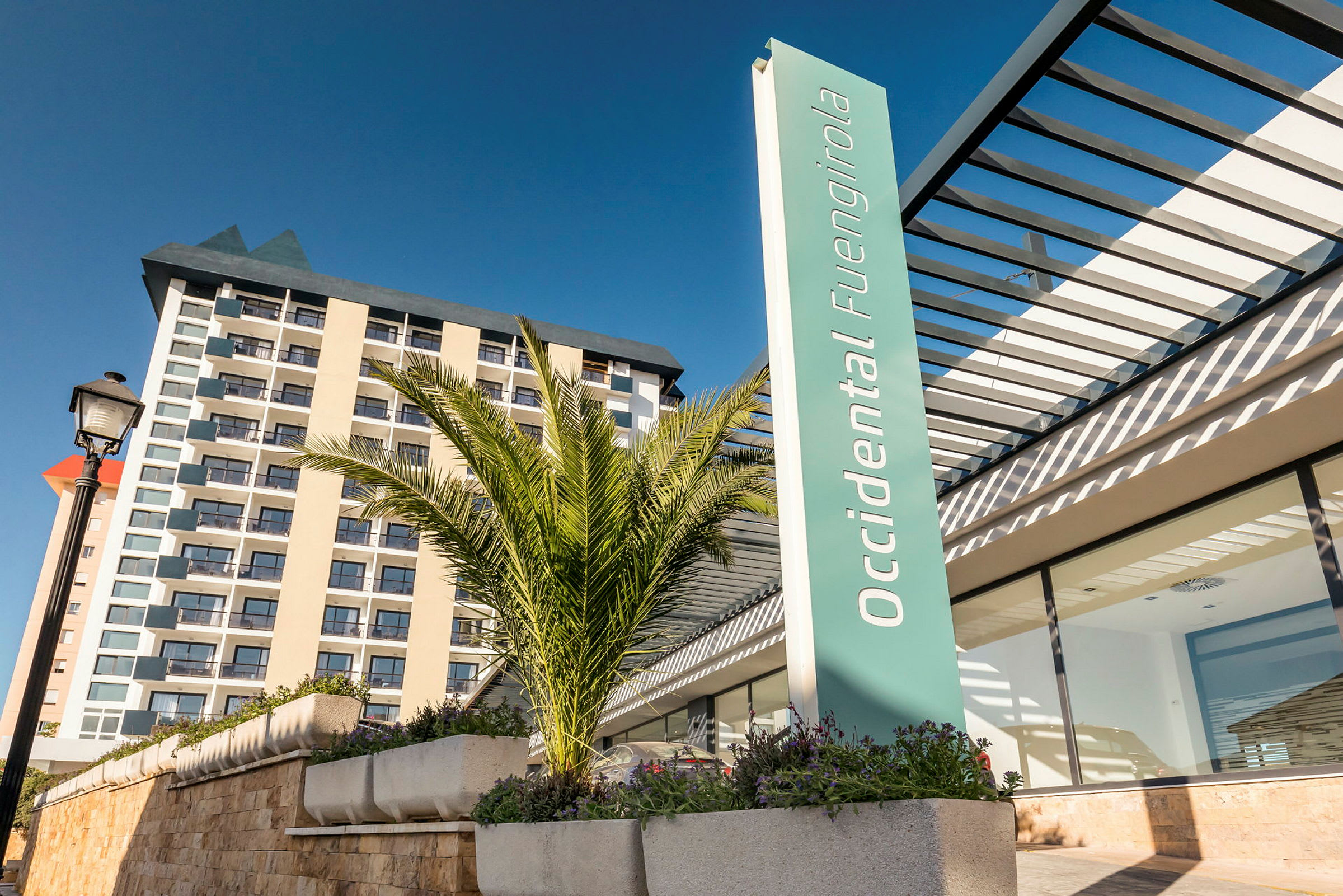 Kuva hotellirakennuksesta modernilla arkkitehtuurilla, jossa kyltti "Occidental Fuengirola" ja etualalla palmuja. (Tekoälyn luoma teksti)