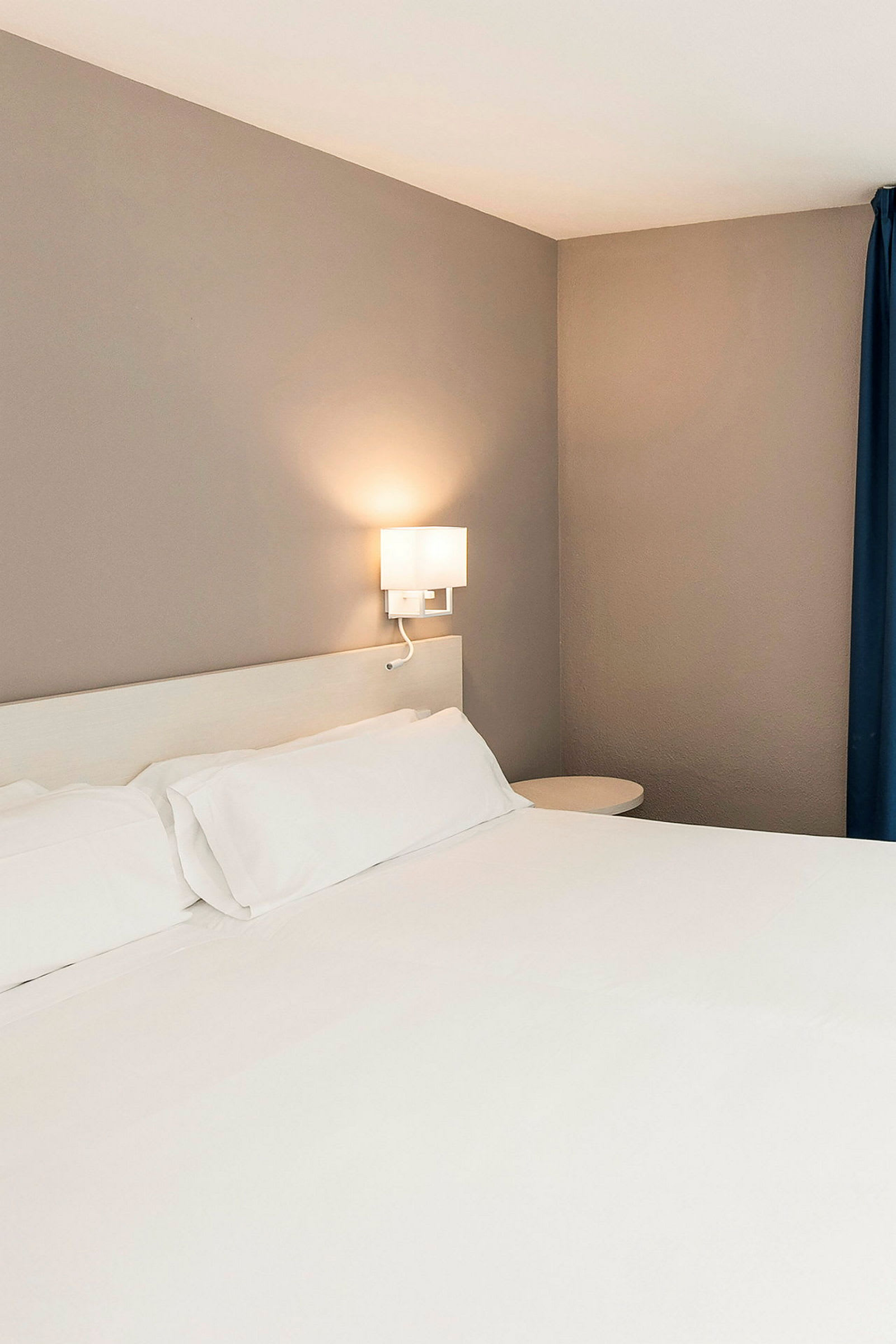 Hotellihuoneen sänky, jossa valkoiset lakanat ja seinävalaisin. (Tekoälyn luoma teksti)