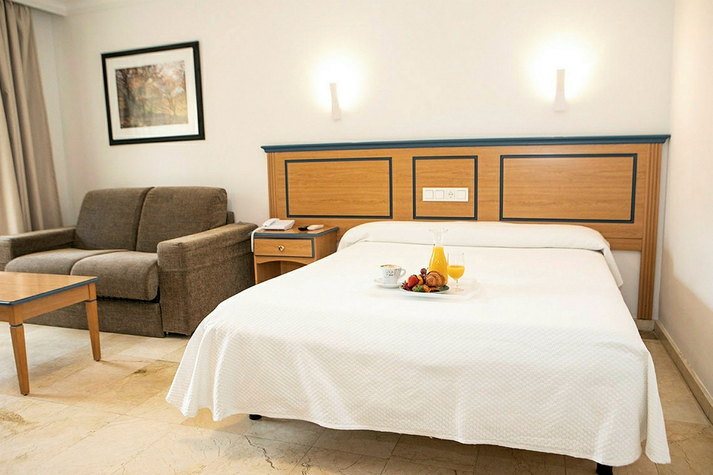 Hotellihuone, jossa pedattu sänky ja sohva. (Tekoälyn luoma teksti)