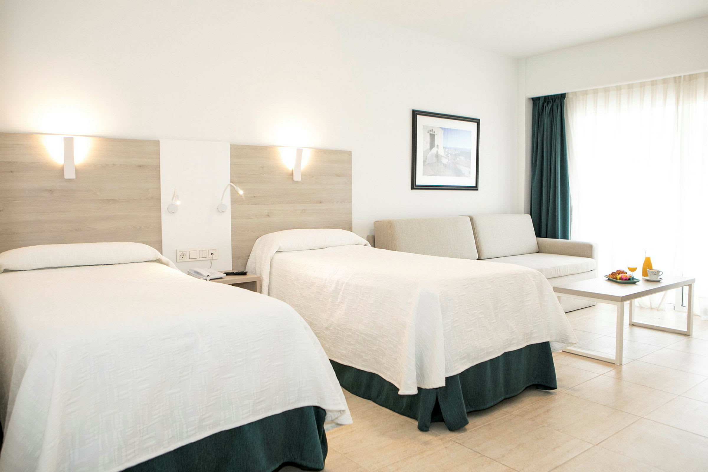 Hotellihuone, jossa on kaksi sänkyä, sohva, pöytä ja aamiaistarjoilu. (Tekoälyn luoma teksti)
