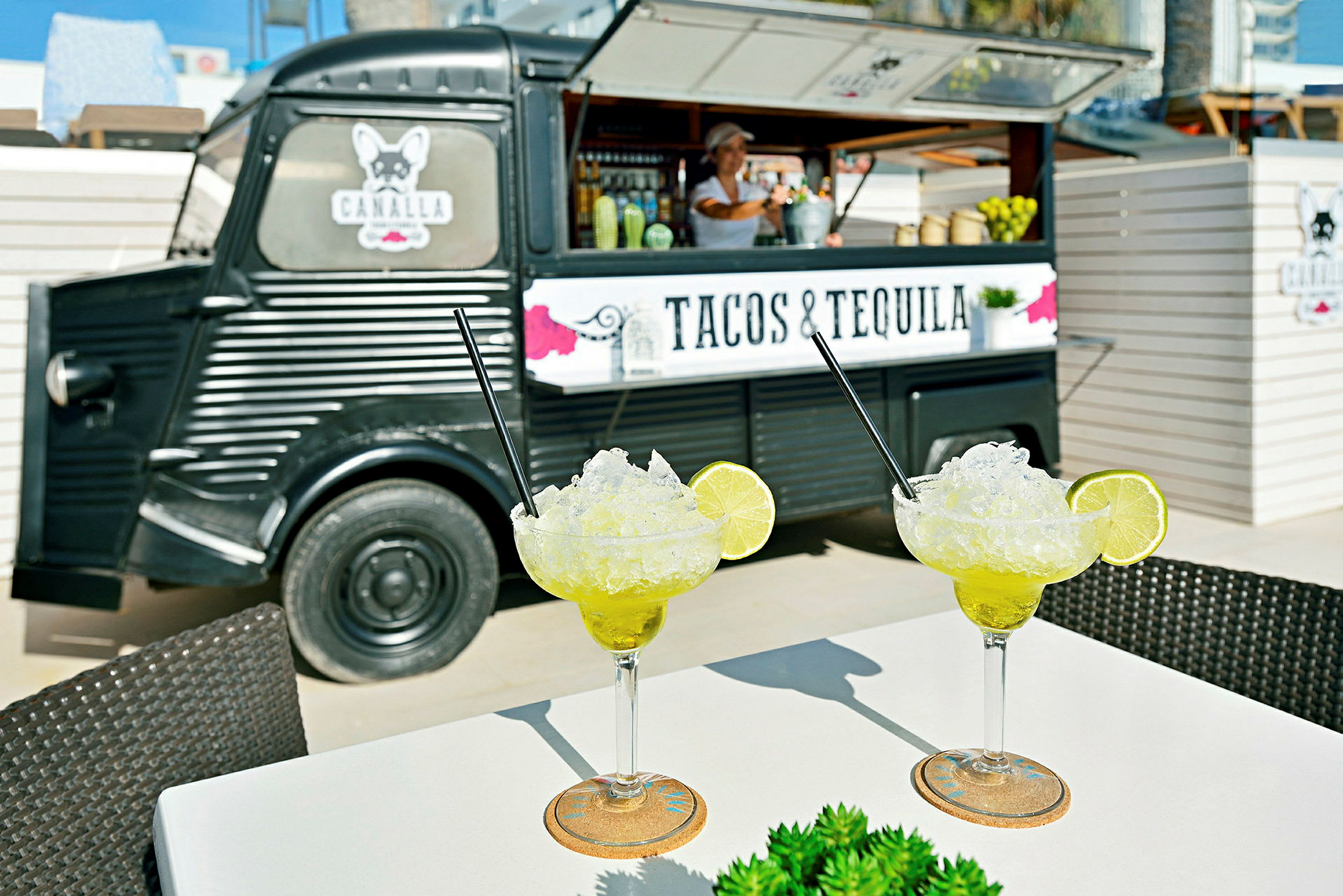 Kaksi margaritalasia on pöydällä ruokakuorma-auton edessä, jossa lukee "Tacos & Tequila". (Tekoälyn luoma teksti)