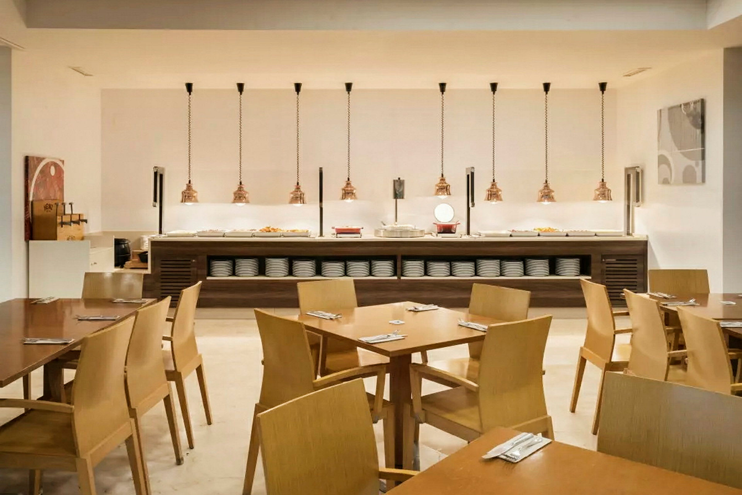 Ruokasali, jossa on puutuoleja ja -pöytiä, buffet tarjoilualue taustalla ja modernit kattovalaisimet. (Tekoälyn luoma teksti)