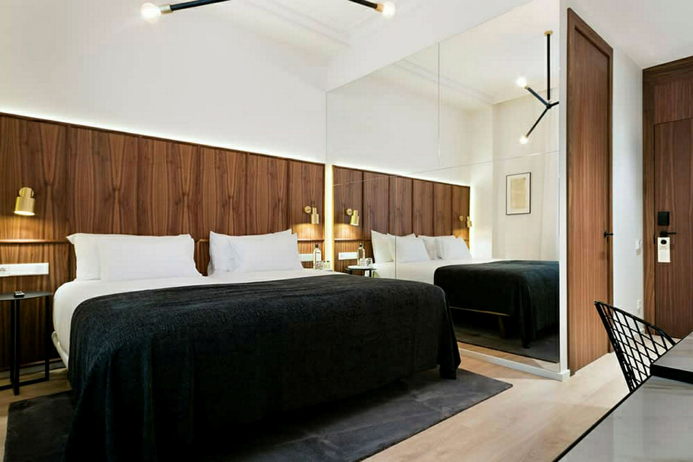 Moderni hotellihuone, jossa suuri sänky, puupaneeliseinät ja peilit, jotka luovat tilavuuden tuntua. (Tekoälyn luoma teksti)