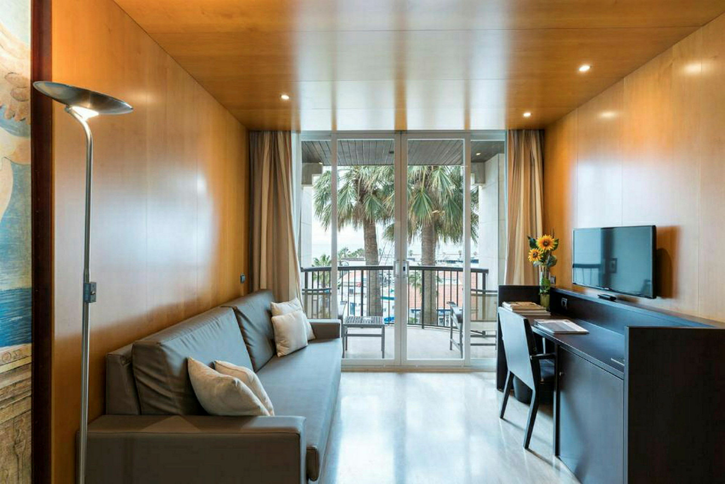 Huone, jossa on sohva, työpöytä, seinä-TV ja ikkunasta näkyvät palmut. (Tekoälyn luoma teksti)
