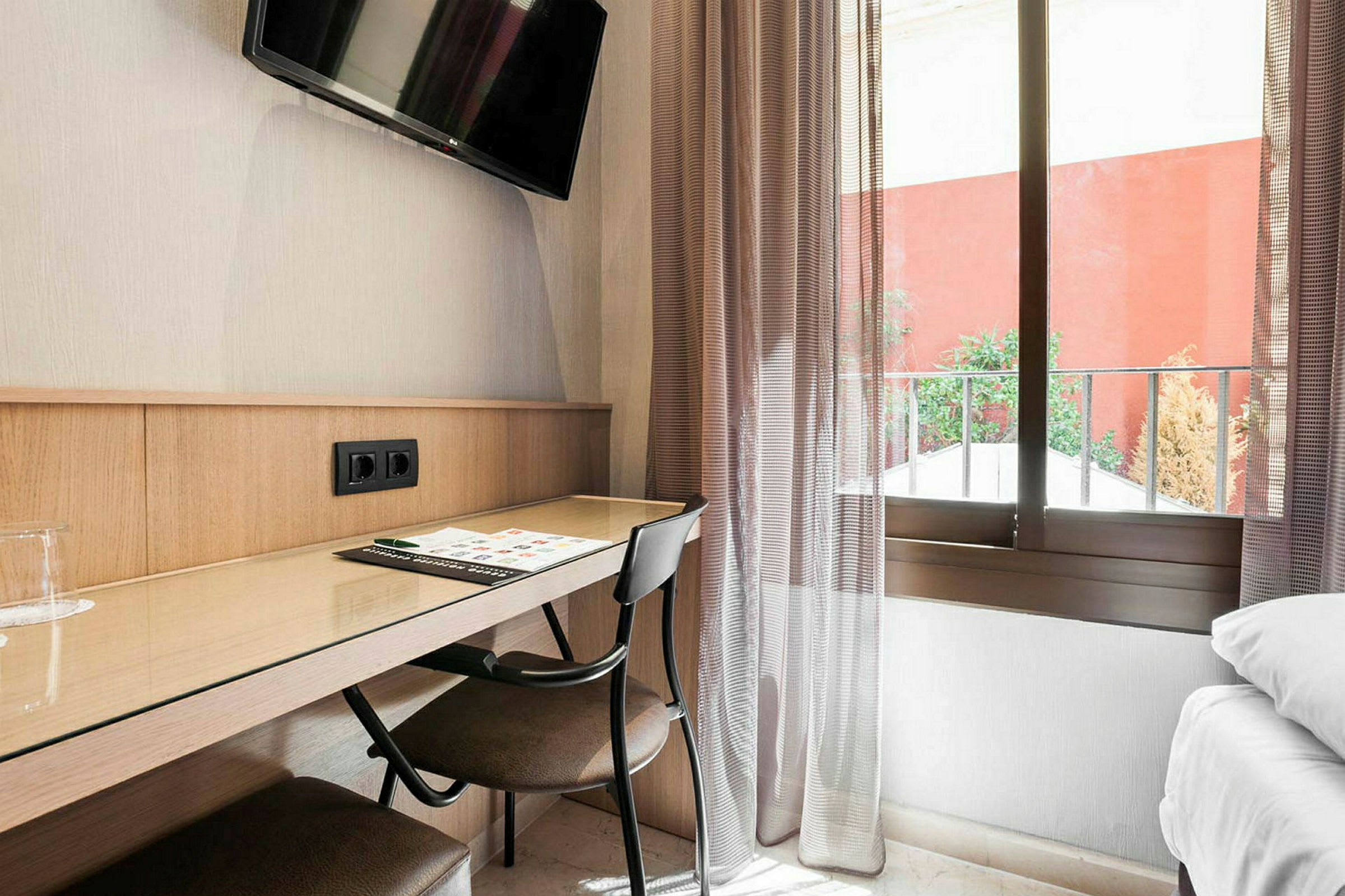 Hotellihuoneen työpöytä tuolilla, kirjoitusvälineillä, seinällä olevalla televisiolla ja taustalla ikkunalla. (Tekoälyn luoma teksti)