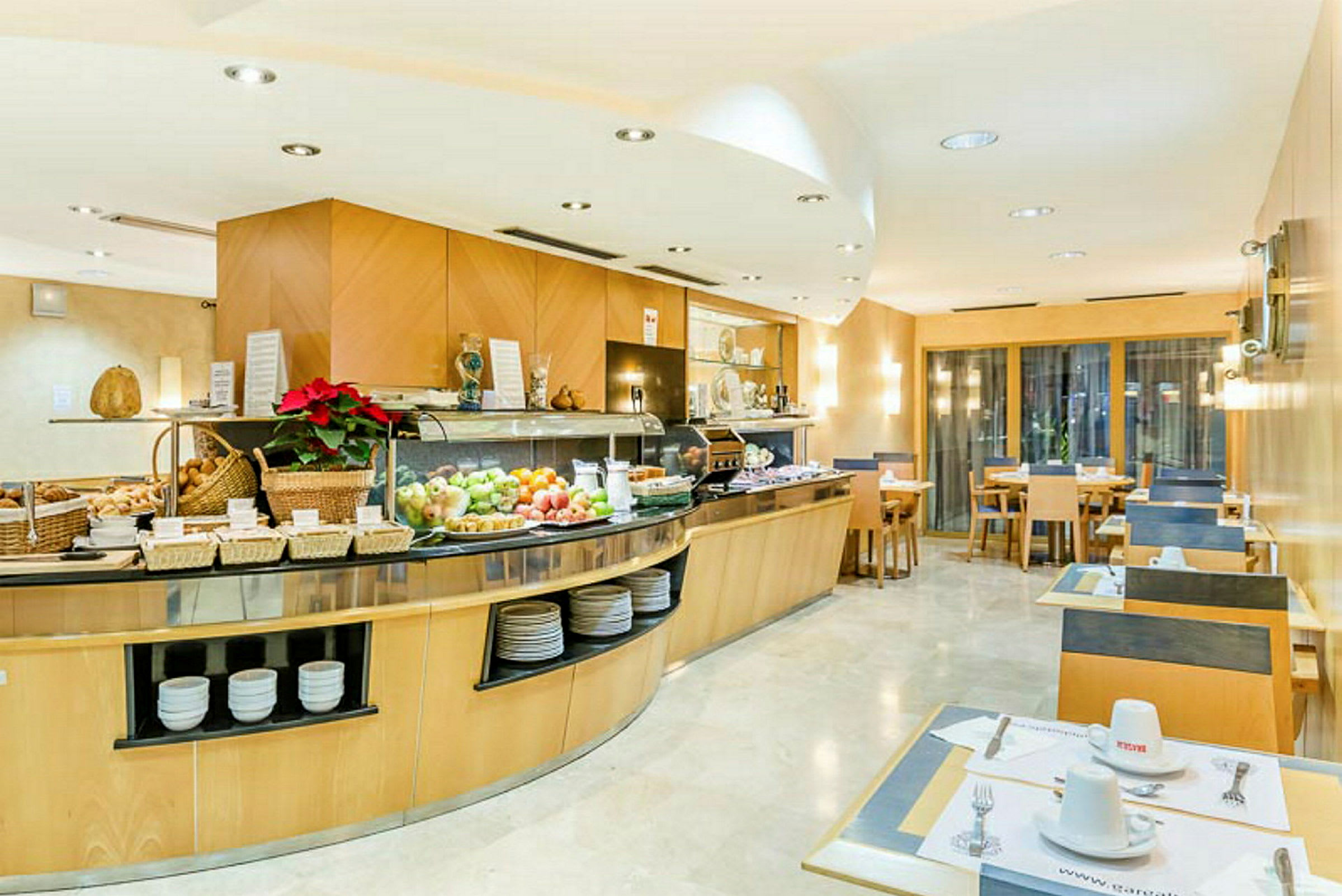 Buffet, jossa hedelmiä, leipää ja juomia valoisassa ja hyvin hoidetussa ruokasalissa. (Tekoälyn luoma teksti)