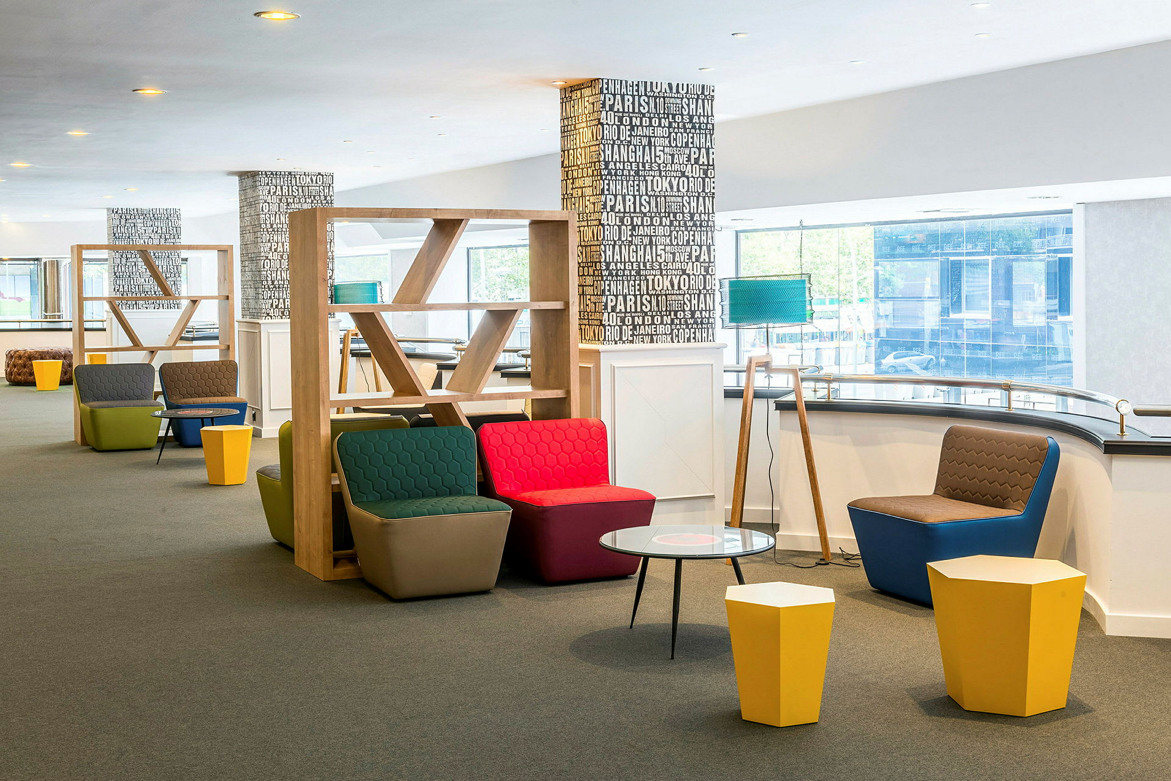 Moderni lounge, jossa on värikkäitä istuimia, pieniä pöytiä ja puisia hyllyjä. (Tekoälyn luoma teksti)
