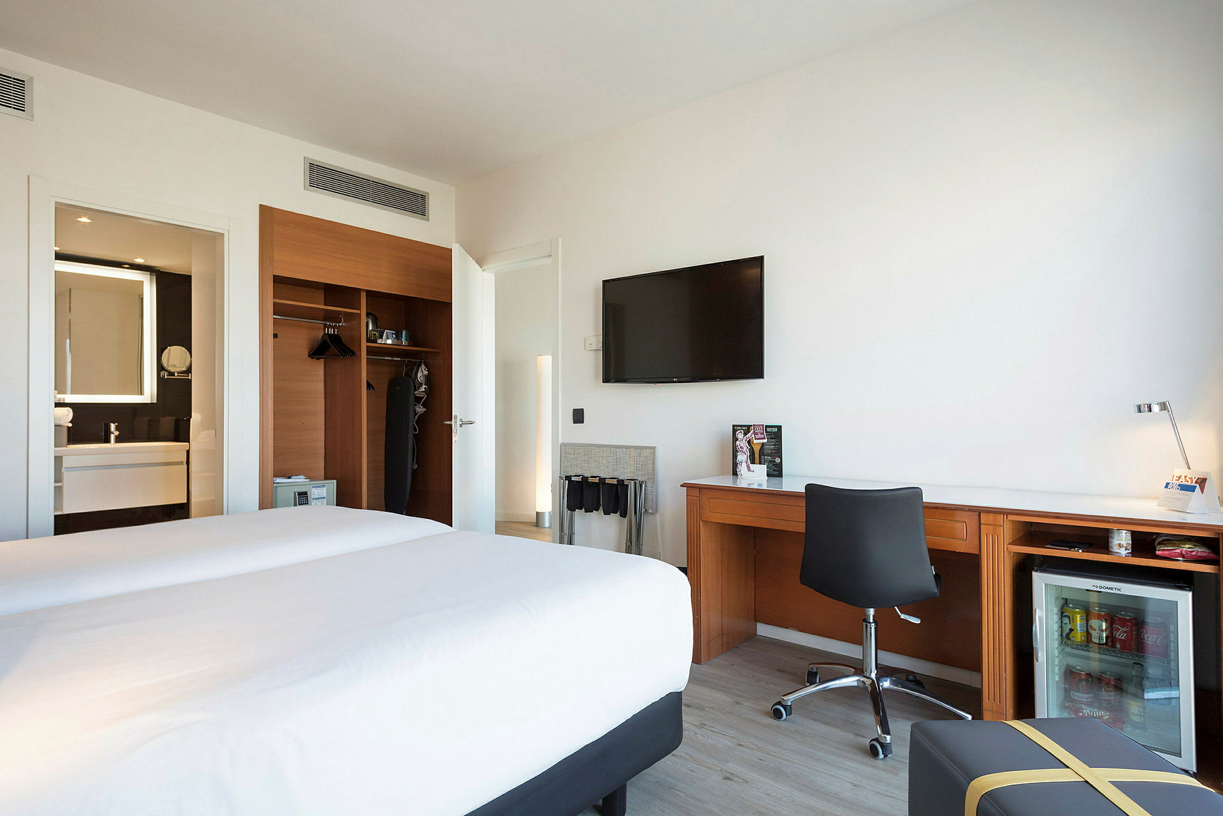Hotellihuone, jossa on kaksi vuodetta, työpöytä, vaatekaappi ja taustalla kylpyhuone. (Tekoälyn luoma teksti)