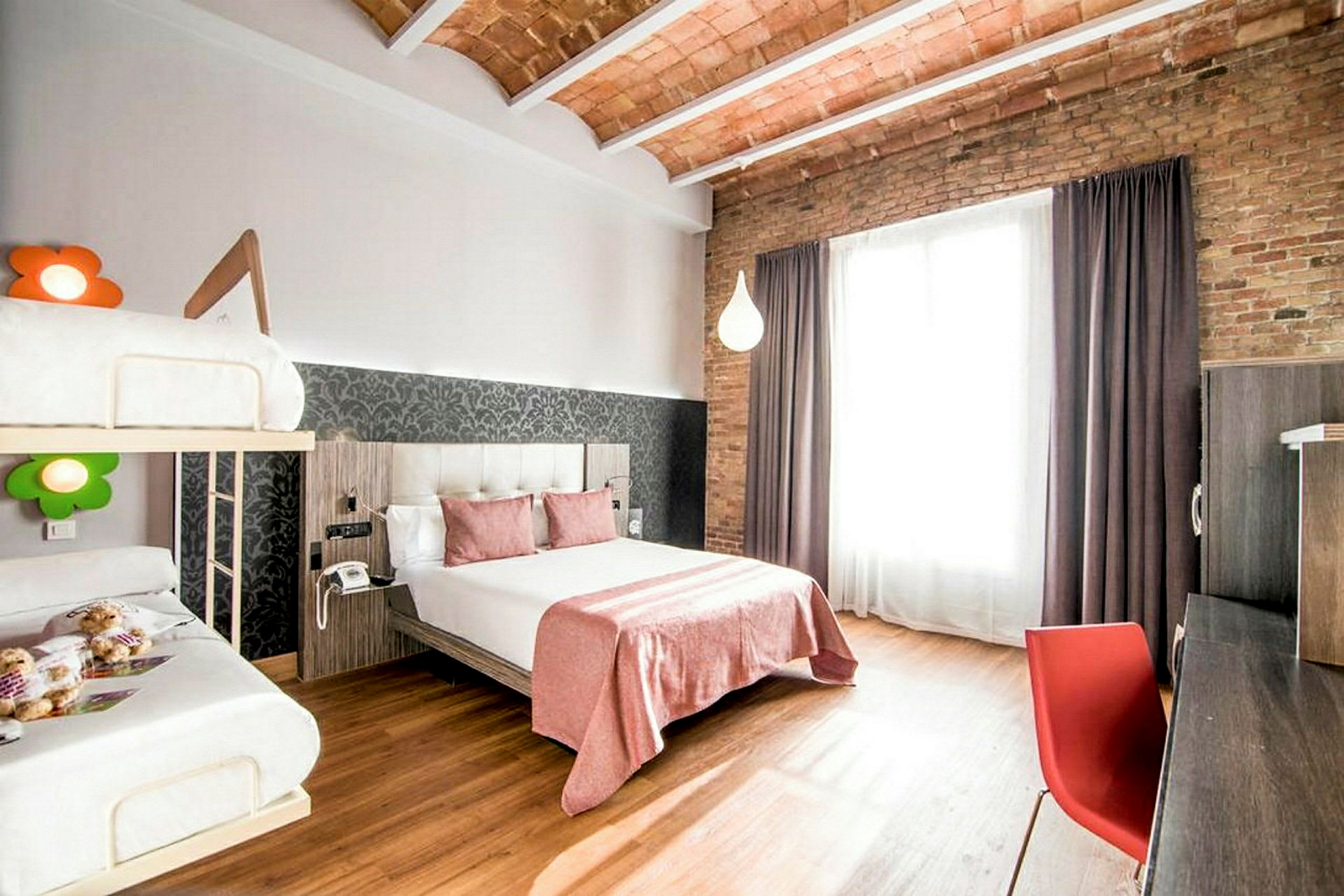 Moderni hotellihuone, jossa on parisänky, kerrossänky, kirjoituspöytä ja suuret ikkunat verhoilla. (Tekoälyn luoma teksti)