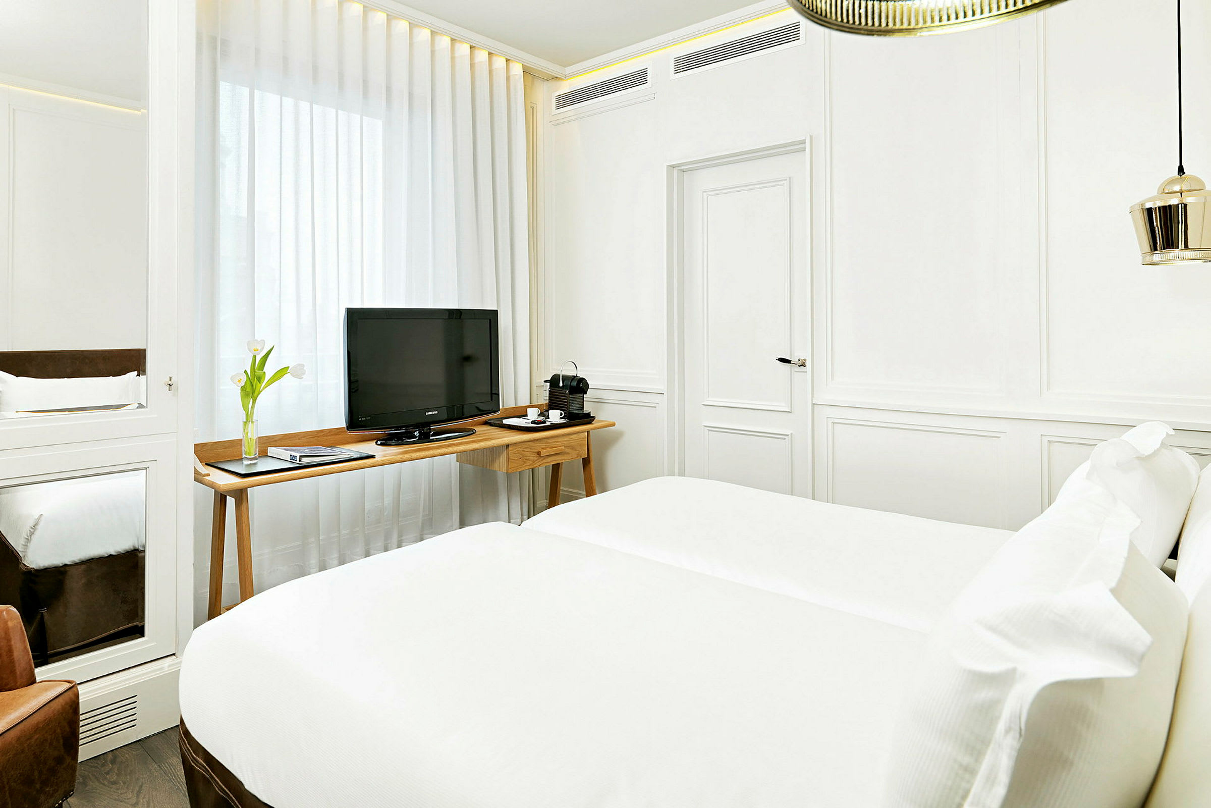 Valoisa hotellihuone, jossa on valkoinen sisustus, parisänky, tv puupöydällä ja kahvinkeitin. (Tekoälyn luoma teksti)