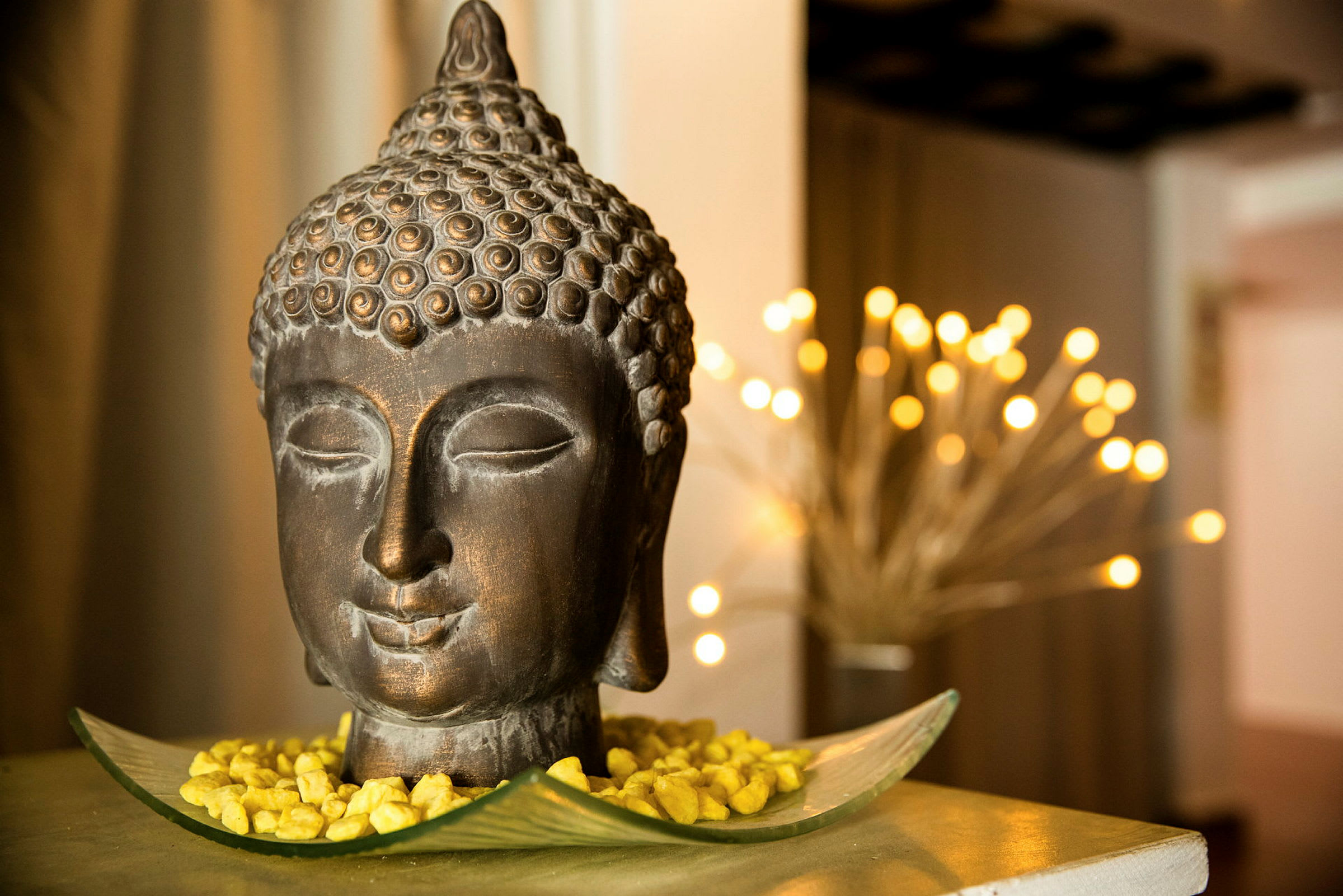 Koristeellinen Buddha-kuvio, joka on asetettu aluslautaselle kultaisilla kivillä. Pehmeä valo taustalla. (Tekoälyn luoma teksti)
