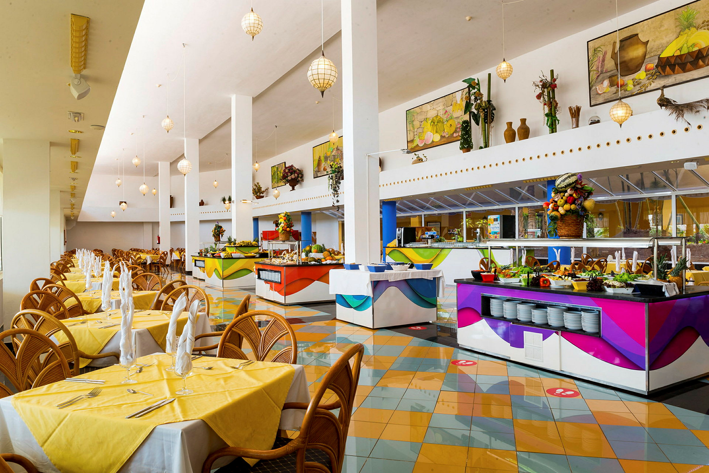 Tilava ravintola, jossa on avarat tilat, keltaiset liinat pöydillä ja useita värikkäitä buffetpisteitä. (Tekoälyn luoma teksti)