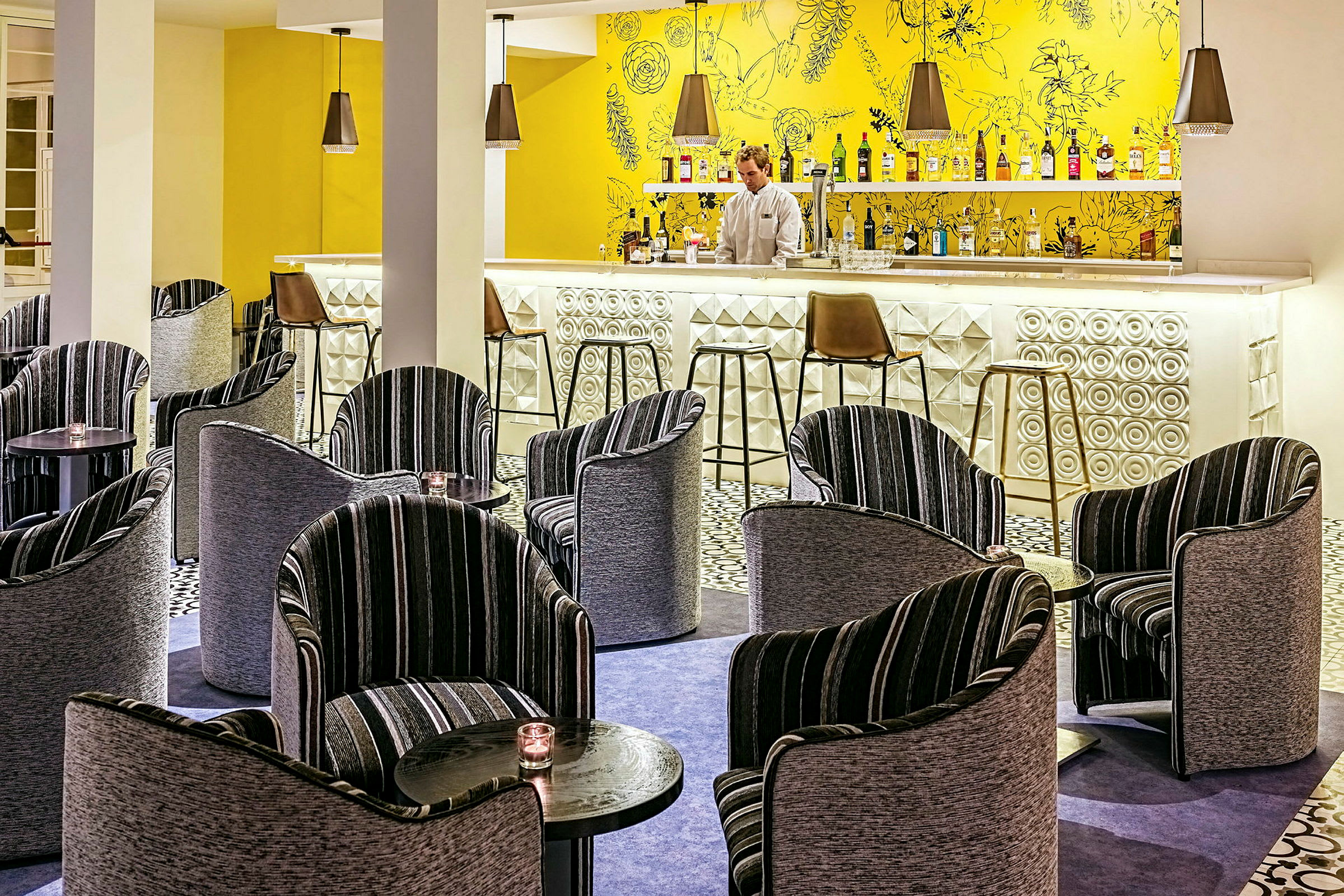 Hotellibaari, jossa on värikäs sisustus, mukaan lukien modernit tuolit ja pienet pöydät. (Tekoälyn luoma teksti)