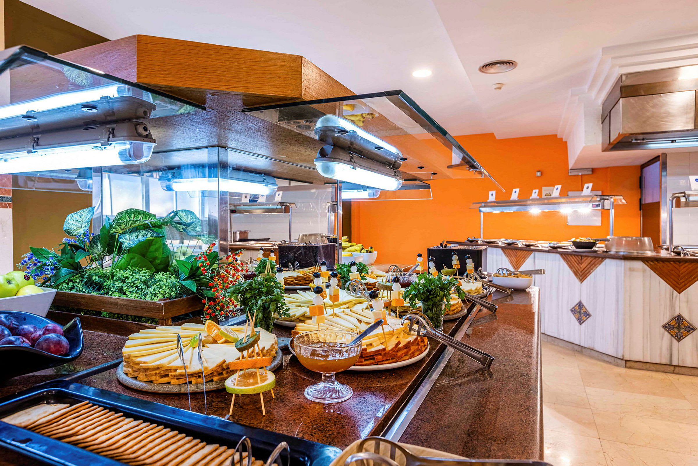 Buffet, jossa erilaisia ruokia, kuten juustoa, keksejä ja hedelmiä, sekä koristekasvit. (Tekoälyn luoma teksti)