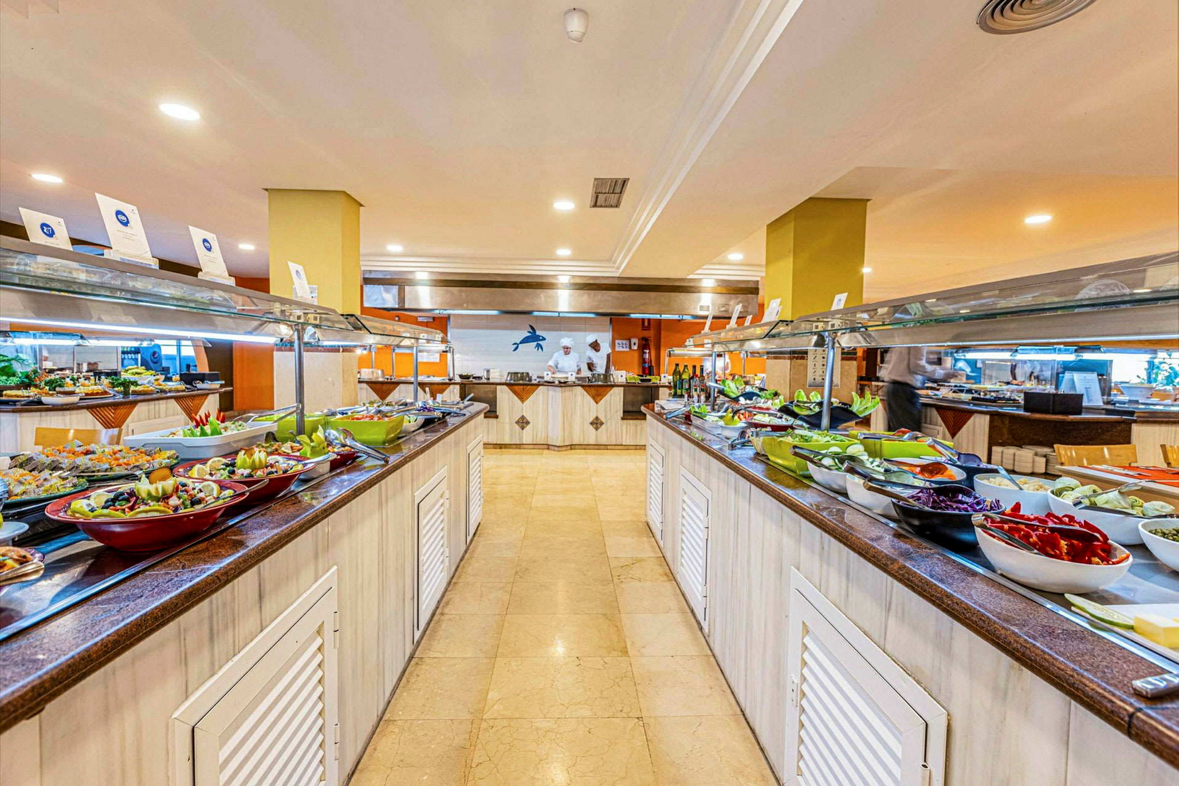 Buffet, jossa on eri ruokia ja salaatteja kahdella pitkällä pöydällä sisätiloissa. (Tekoälyn luoma teksti)