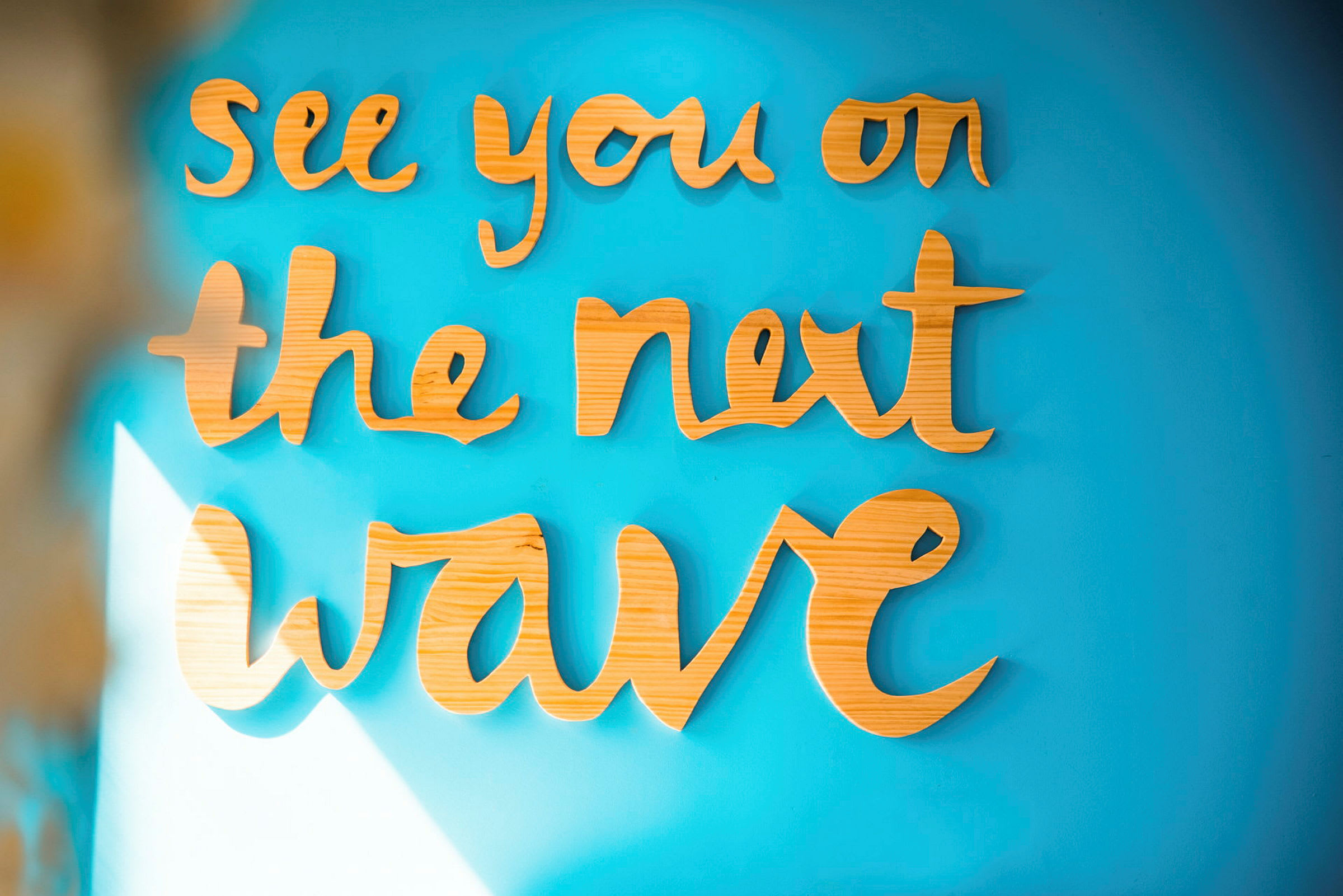 Puusta valmistettu teksti: "See you on the next wave" sinisellä seinällä. (Tekoälyn luoma teksti)