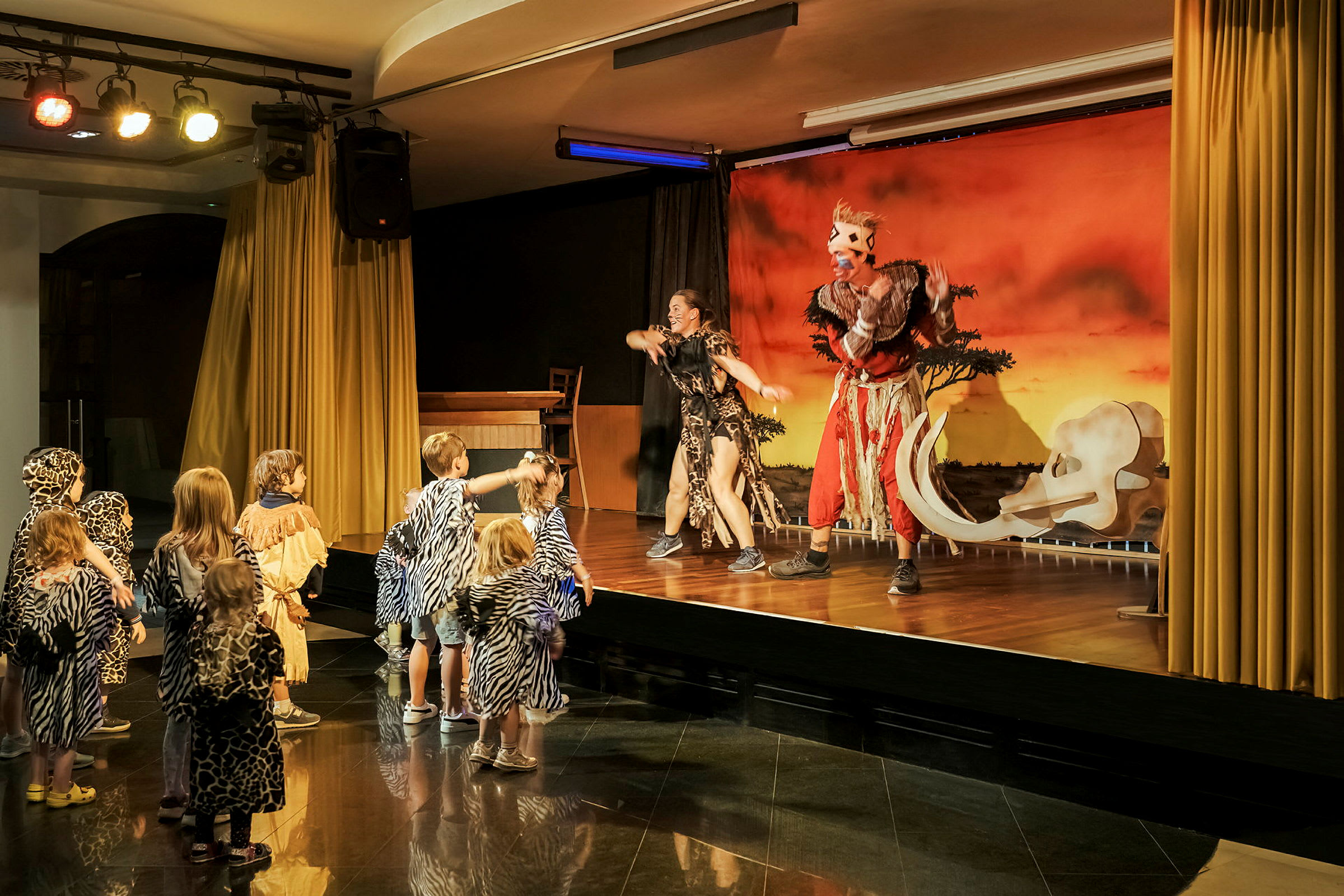 Lapset seisovat lavan edessä, jossa kaksi henkilöä esiintyy eläinaiheisissa puvuissa. (Tekoälyn luoma teksti)