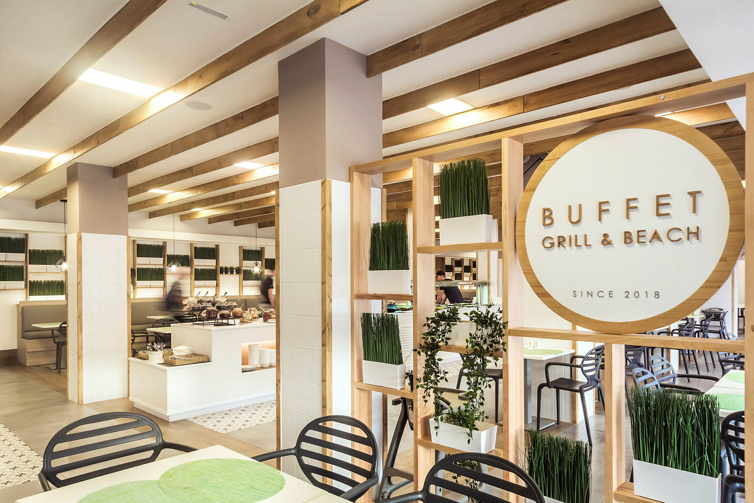 Ravintolan sisätilat, jossa on buffet, puuyksityiskohtia, kasvikoristeita ja kyltti "Buffet Grill & Beach". (Tekoälyn luoma teksti)