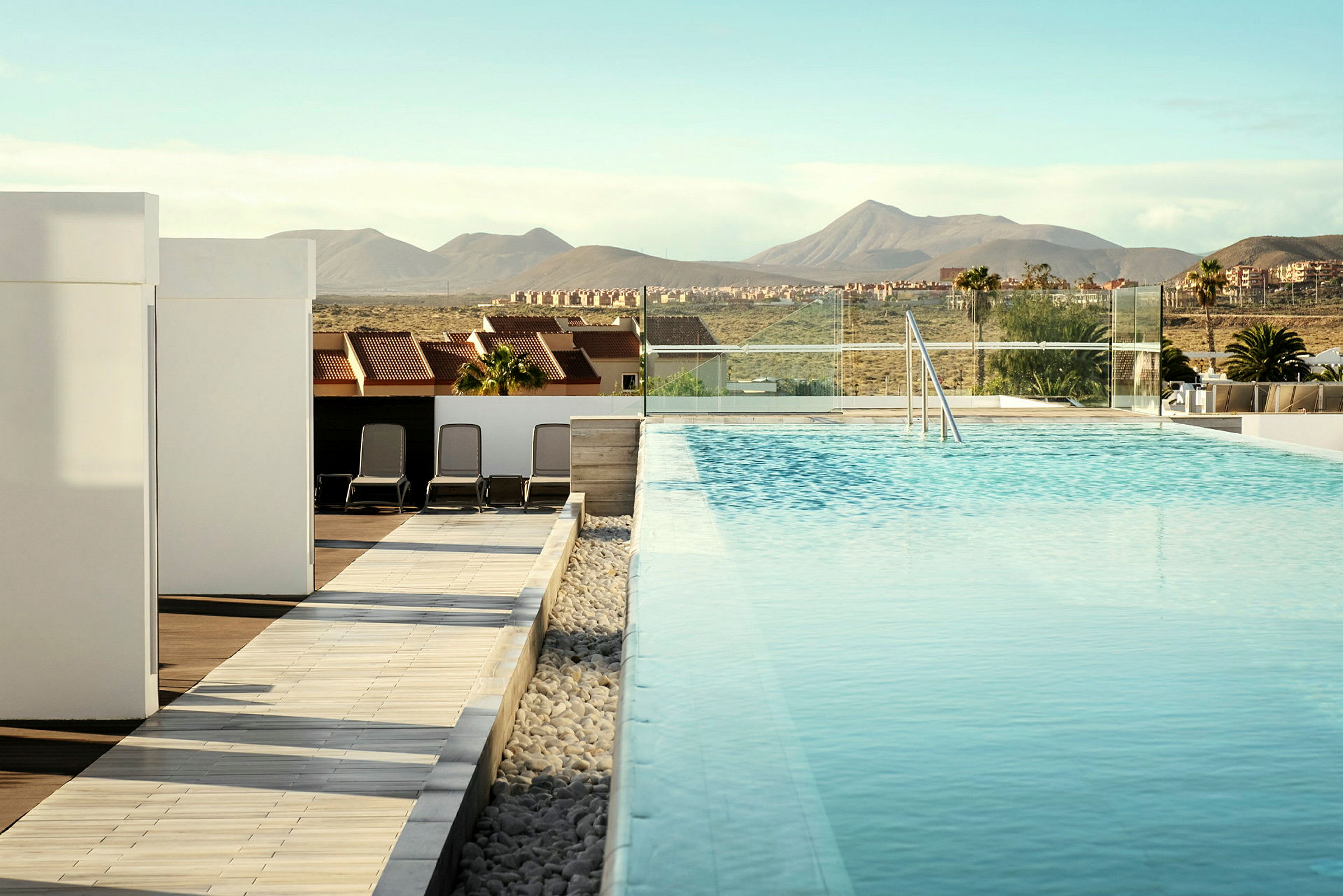 Uima-allas, jota ympäröivät modernit rakennukset ja aurinkotuolit, taustalla vuoria. (Tekoälyn luoma teksti)
