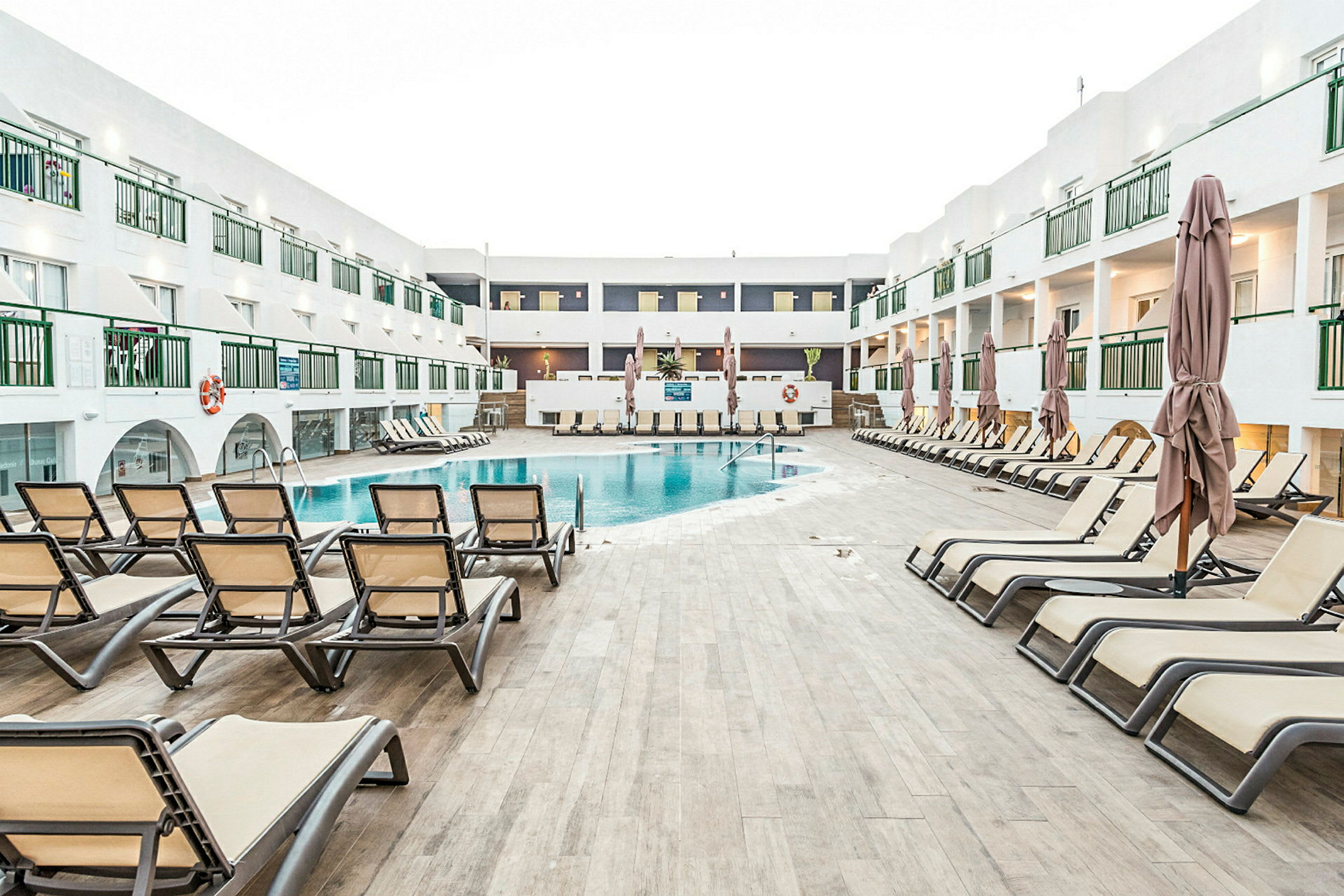 Kuva, jossa on uima-allas, jota ympäröivät aurinkotuolit, ja taustalla hotellikompleksi. (Tekoälyn luoma teksti)