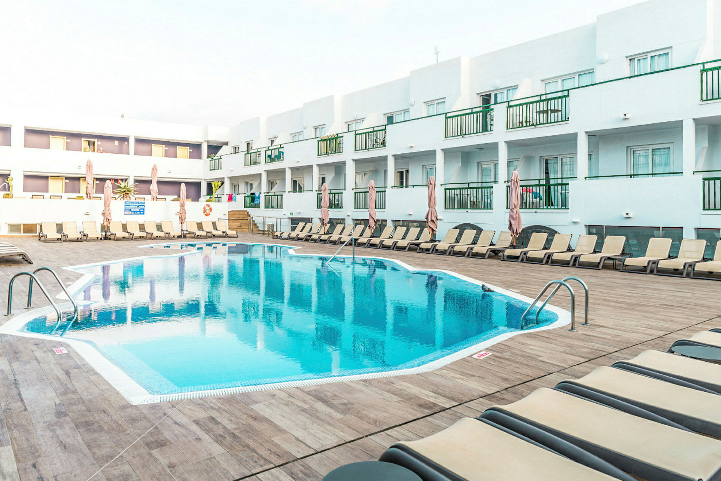 Ulkouima-allas hotellilla, ympärillä aurinkotuoleja ja varjoja, taustalla valkoisia rakennuksia. (Tekoälyn luoma teksti)