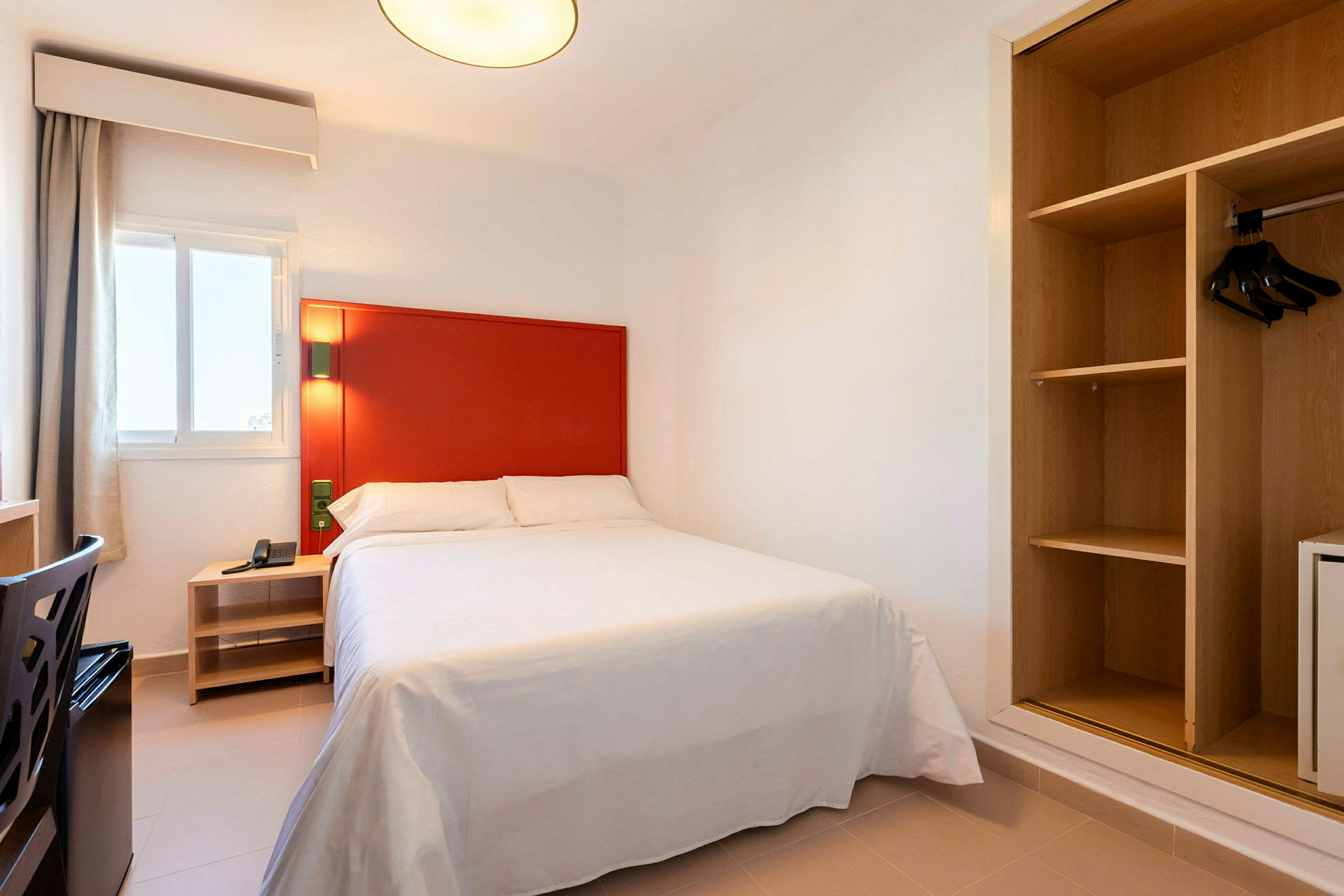 Kuva hotellihuoneesta, jossa on sänky, punainen sängynpääty ja avoin vaatekaappi. (Tekoälyn luoma teksti)