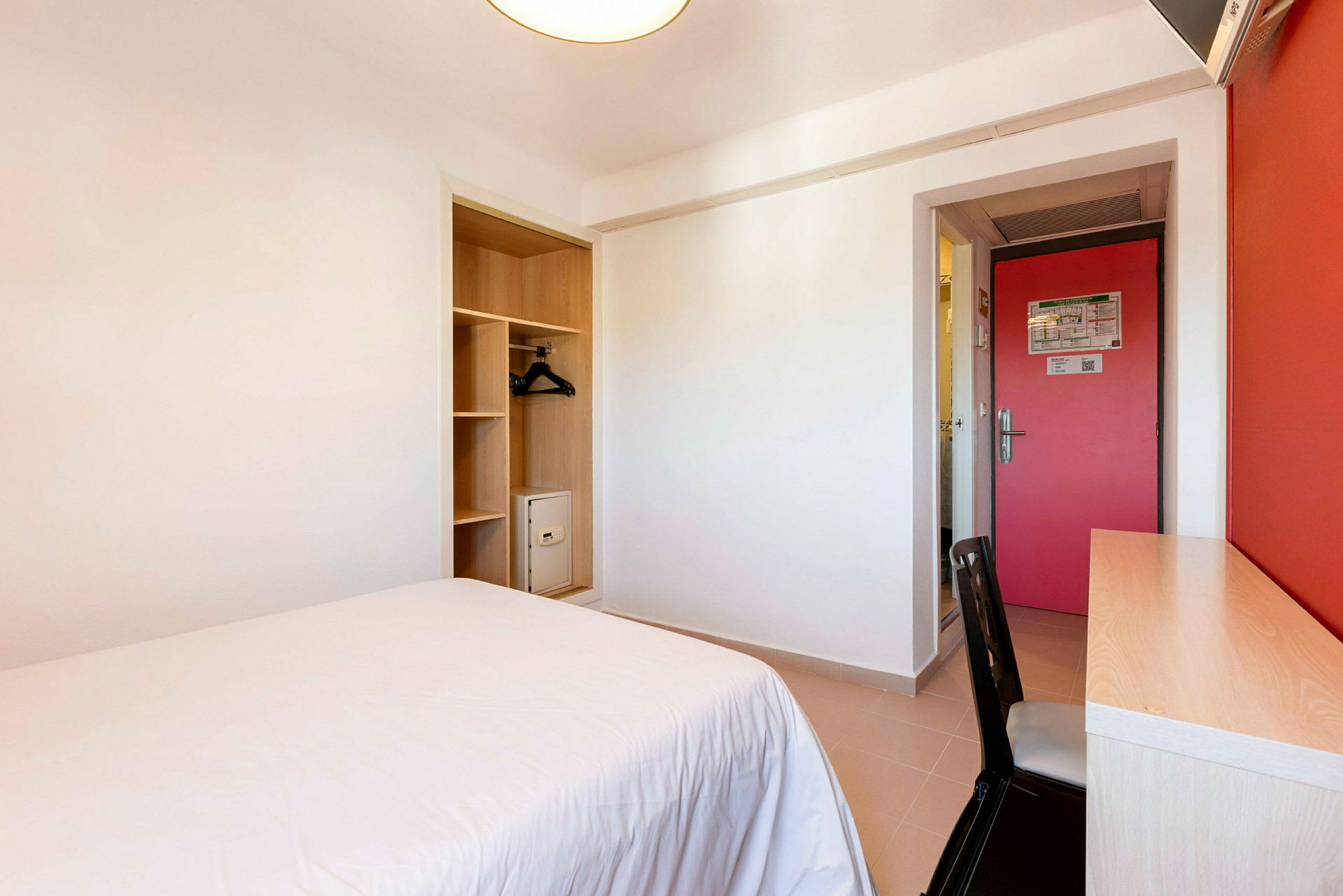 Hotellihuone, jossa on sänky, kirjoituspöytä ja vaatekaappi. (Tekoälyn luoma teksti)