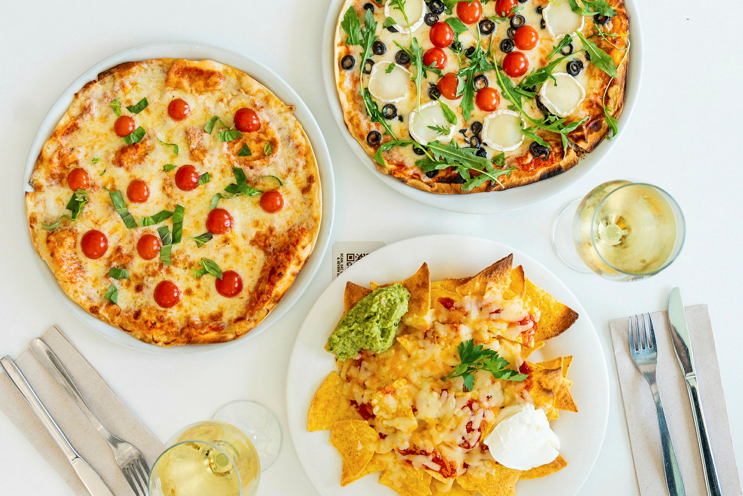 Kaksi pizzaa eri täytteillä ja lautanen nachoja guacamolella ja smetanalla. (Tekoälyn luoma teksti)