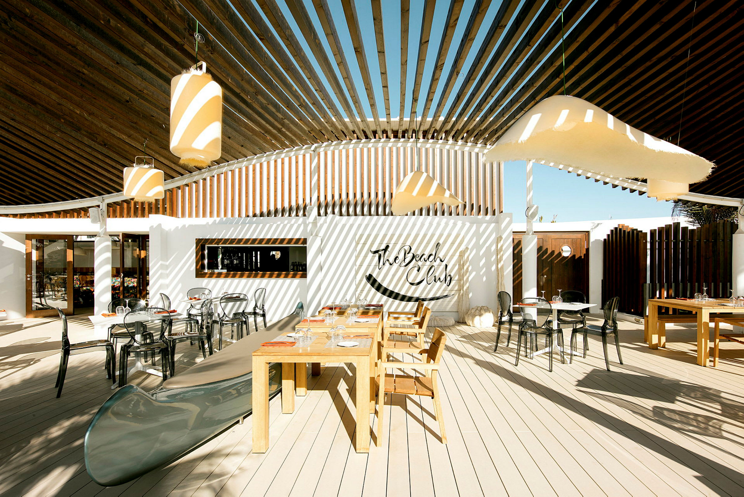 Ulkotila, jossa pöytiä ja tuoleja, sekä koristelua The Beach Club -kyltillä. (Tekoälyn luoma teksti)
