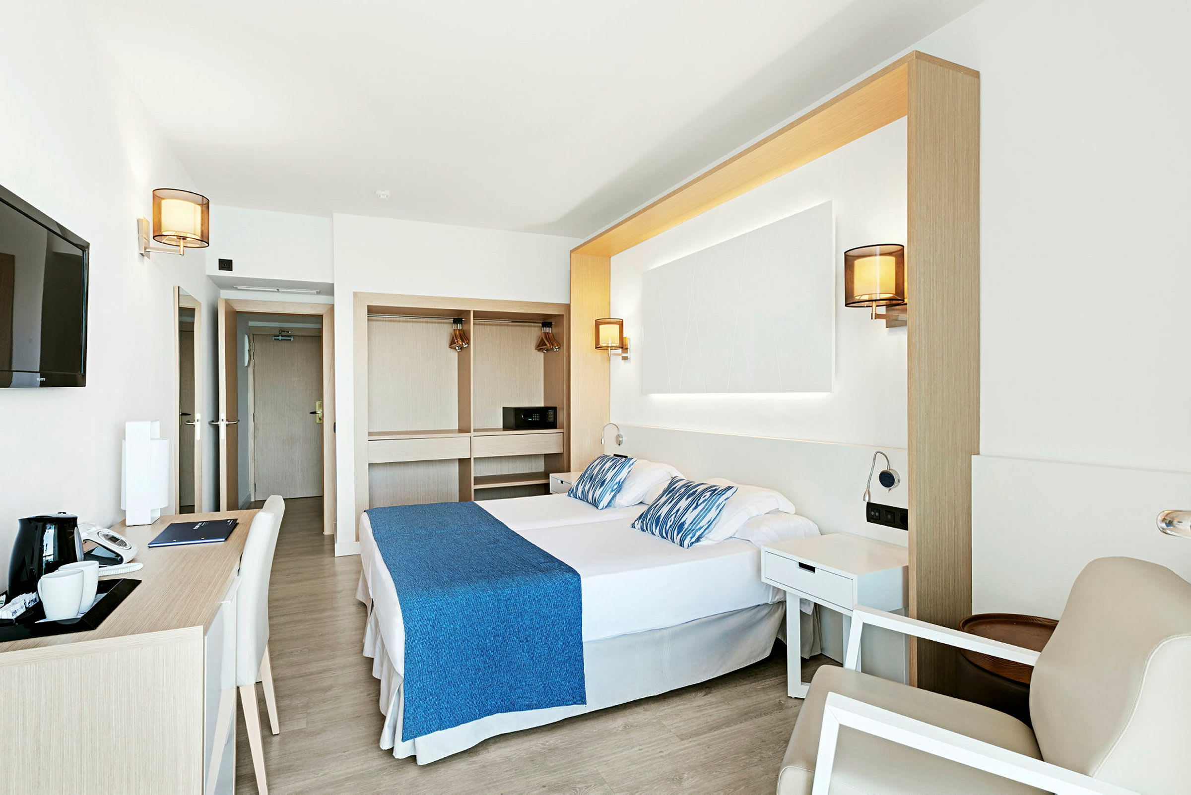 Vaalea ja moderni hotellihuone, jossa parisänky, työpöytä ja vaatekaappi. (Tekoälyn luoma teksti)