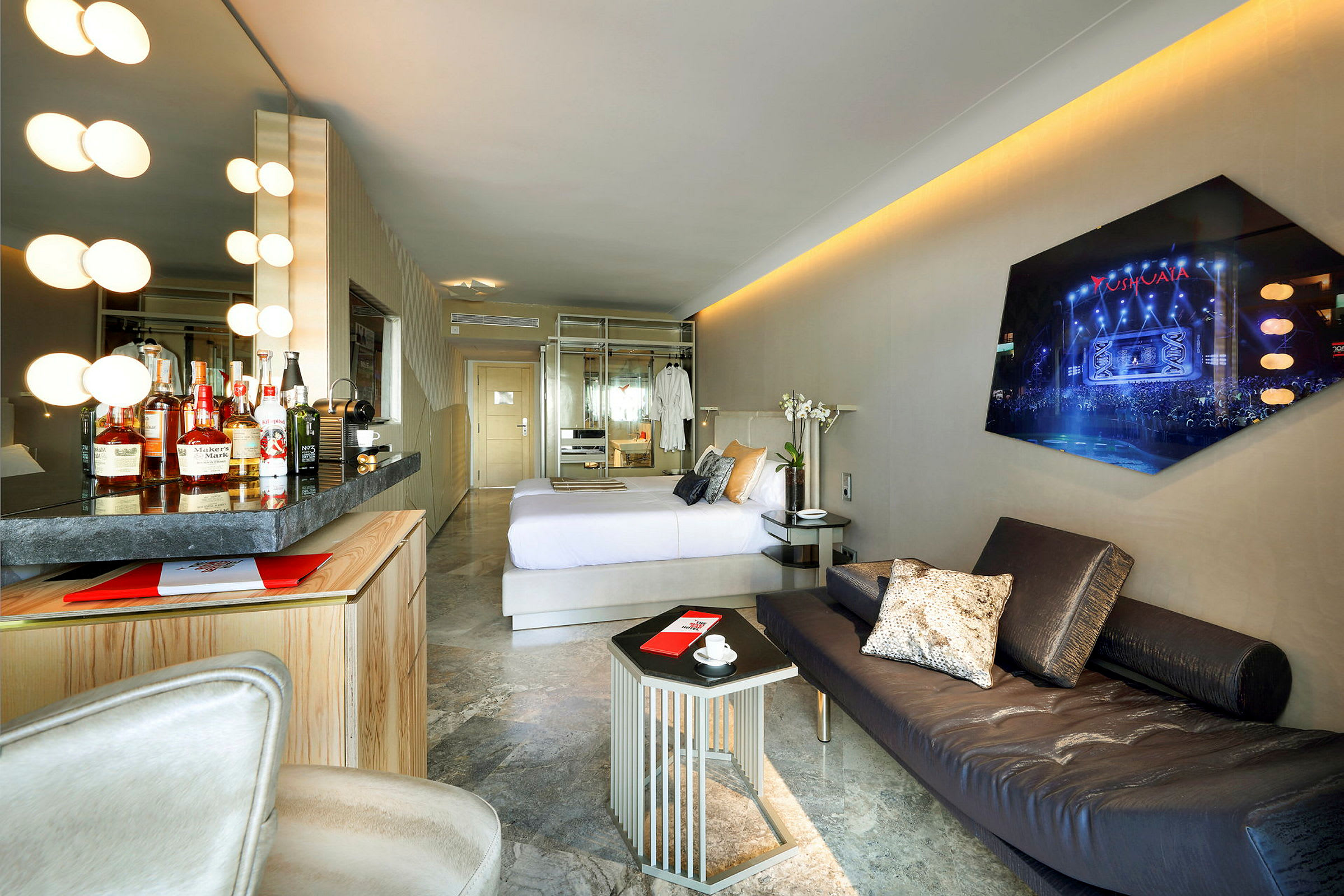 Kuva modernisti suunnitellusta hotellihuoneesta, joka sisältää mukavan sängyn, minibaarin, sohvan ja seinätelevision. (Tekoälyn luoma teksti)