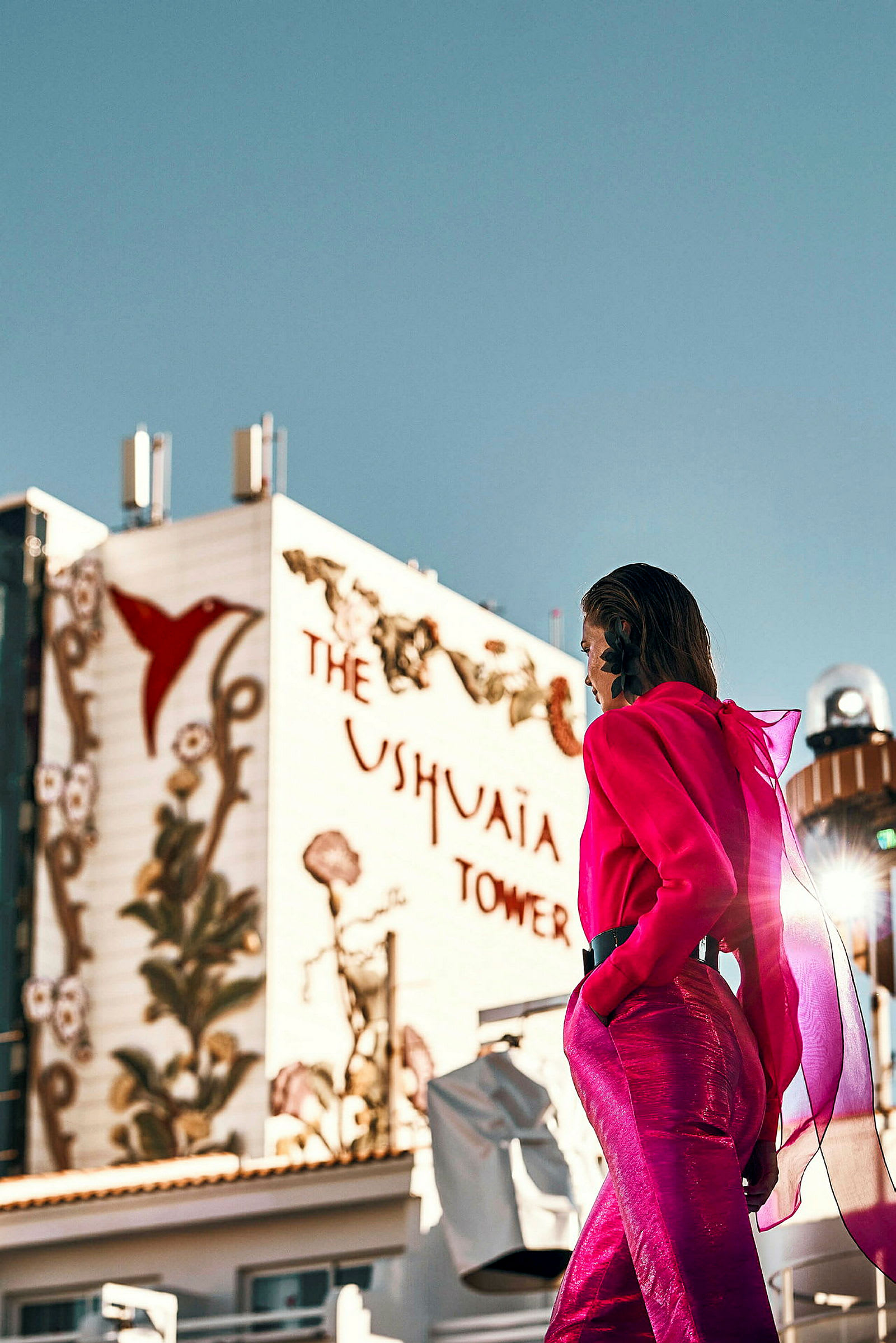 Henkilö vaaleanpunaisessa asussa rakennuksen edessä, jossa lukee 'Ushuaia Tower' ja koristeita. (Tekoälyn luoma teksti)