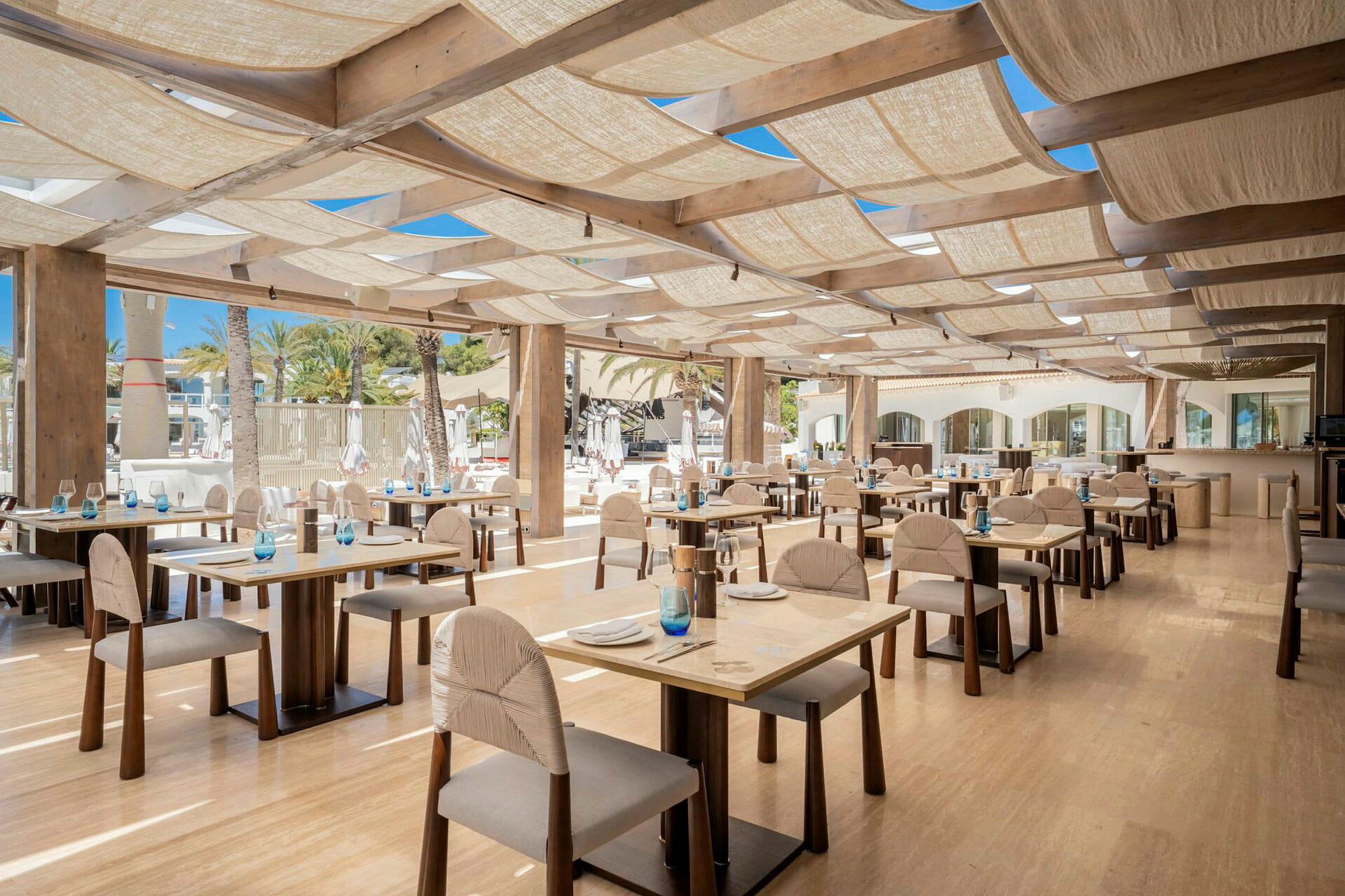 Ravintola, jossa on puupöytiä ja tuoleja, valaistu hyvin luonnonvalolla. (Tekoälyn luoma teksti)