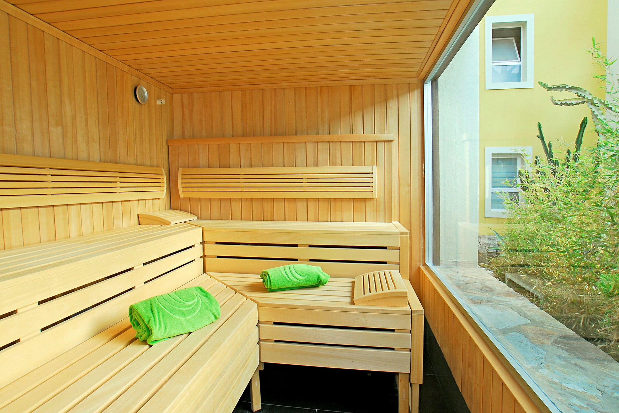 Puinen sauna vihreillä pyyhkeillä ja suuret ikkunat, jotka avautuvat sisäpihalle. (Tekoälyn luoma teksti)