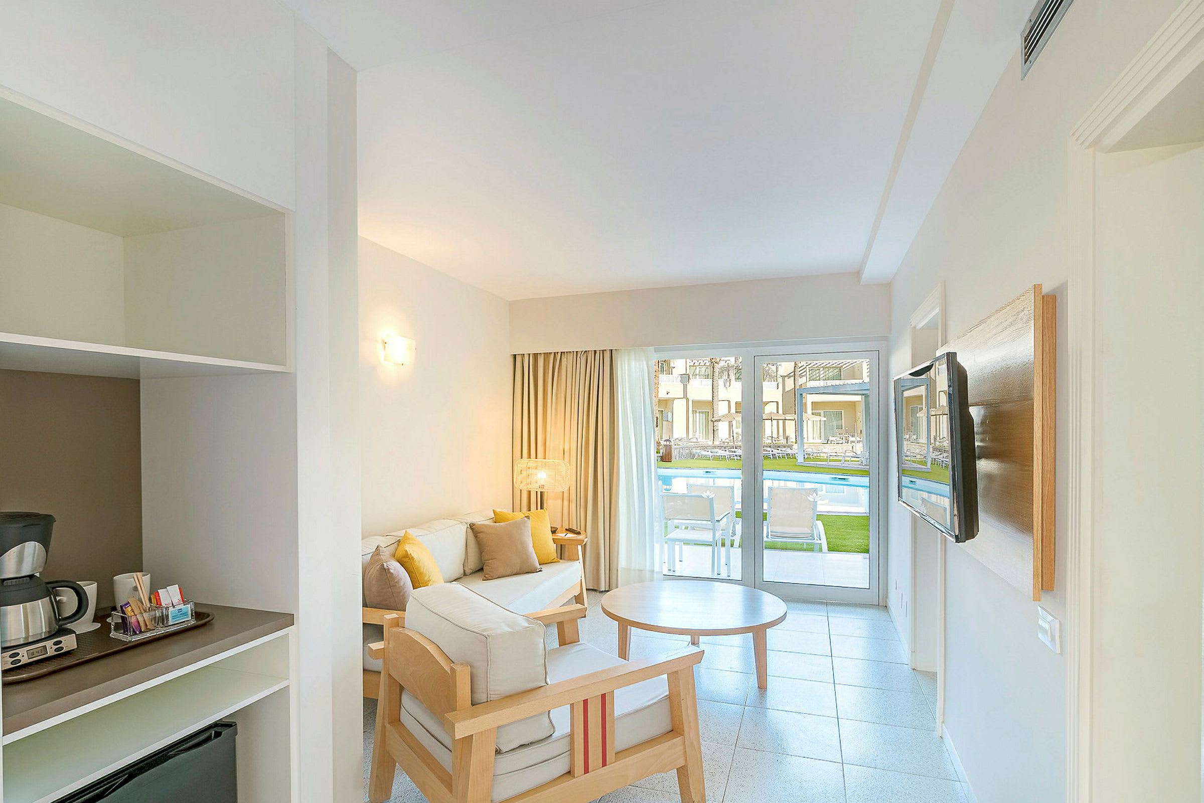 Hotellihuone, jossa istuinryhmä ja näkymä uima-altaalle lasioven kautta. (Tekoälyn luoma teksti)