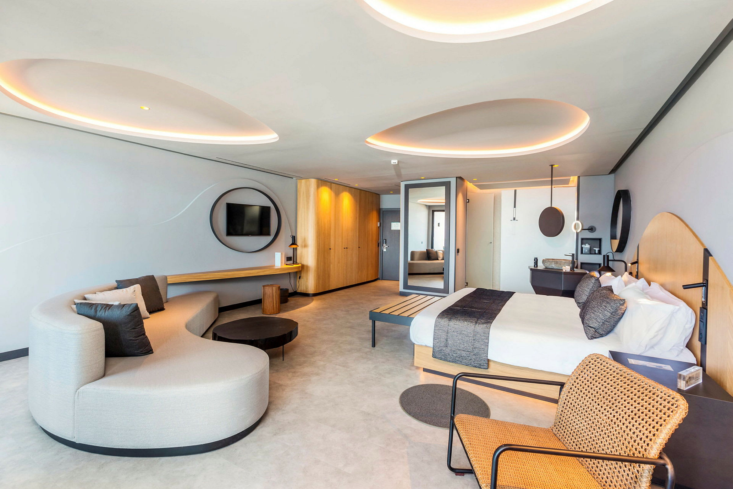 Moderni hotellihuone, jossa sänky, sohva ja punottu tuoli. (Tekoälyn luoma teksti)