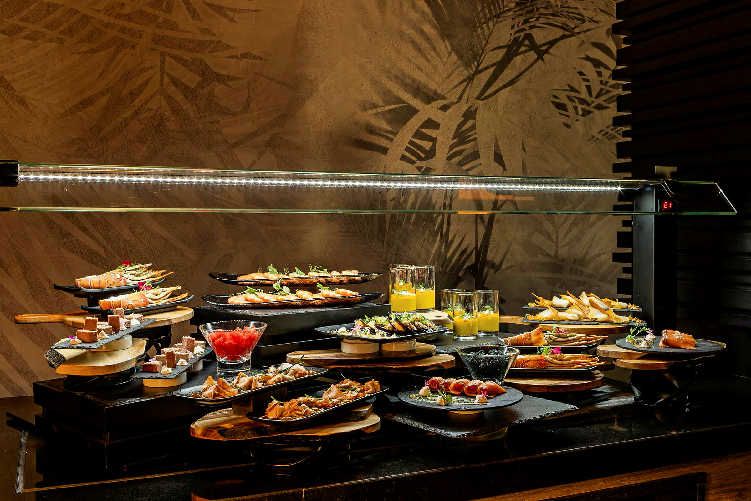 Buffetpöytä, jossa on erilaisia ruokia ja jälkiruokia lautasilla ja laseissa lasikuvun alla. (Tekoälyn luoma teksti)