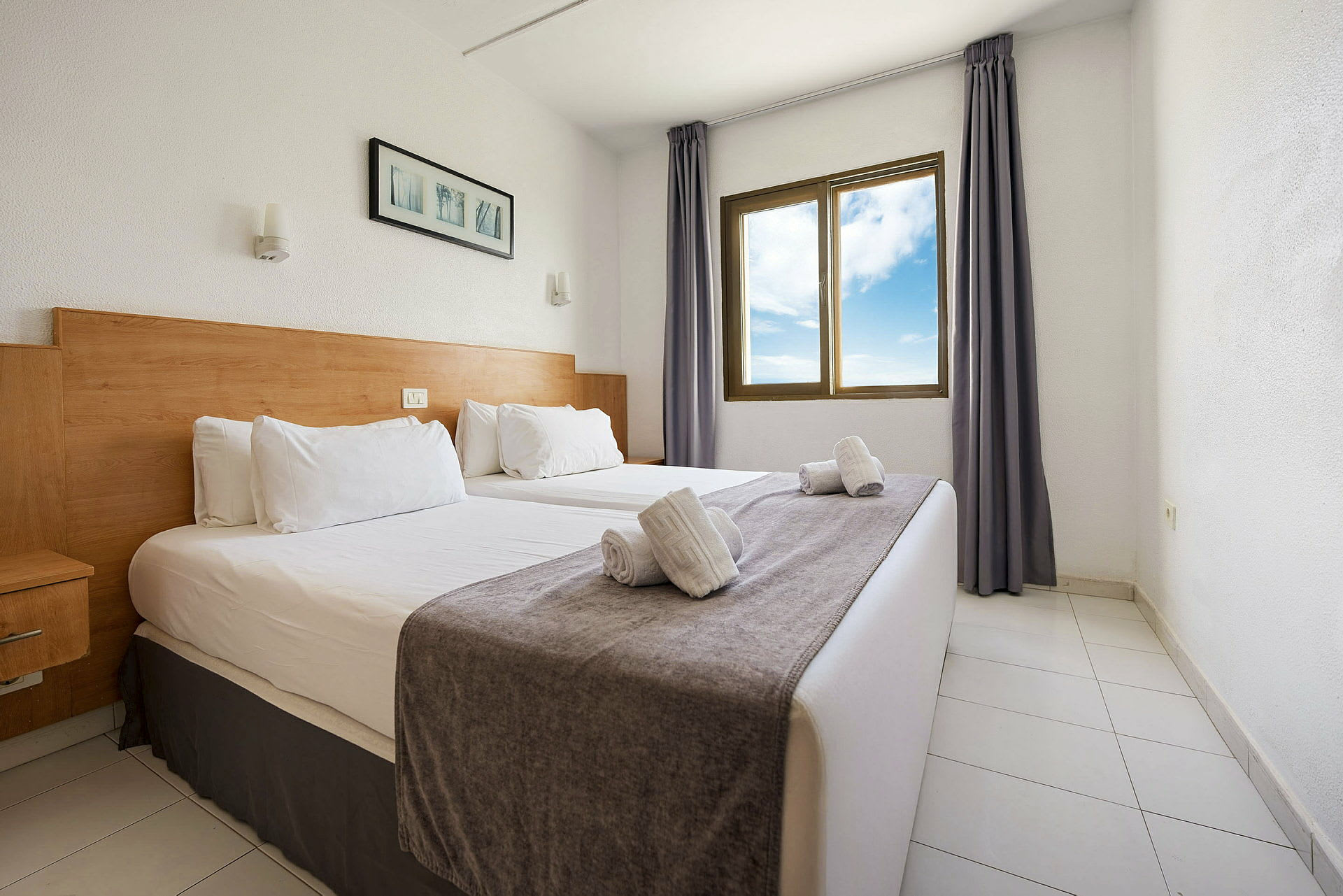 Hotellihuone, jossa on kaksi yhden hengen vuodetta, ikkuna näkymällä ja yksinkertaisia koristuksia. (Tekoälyn luoma teksti)