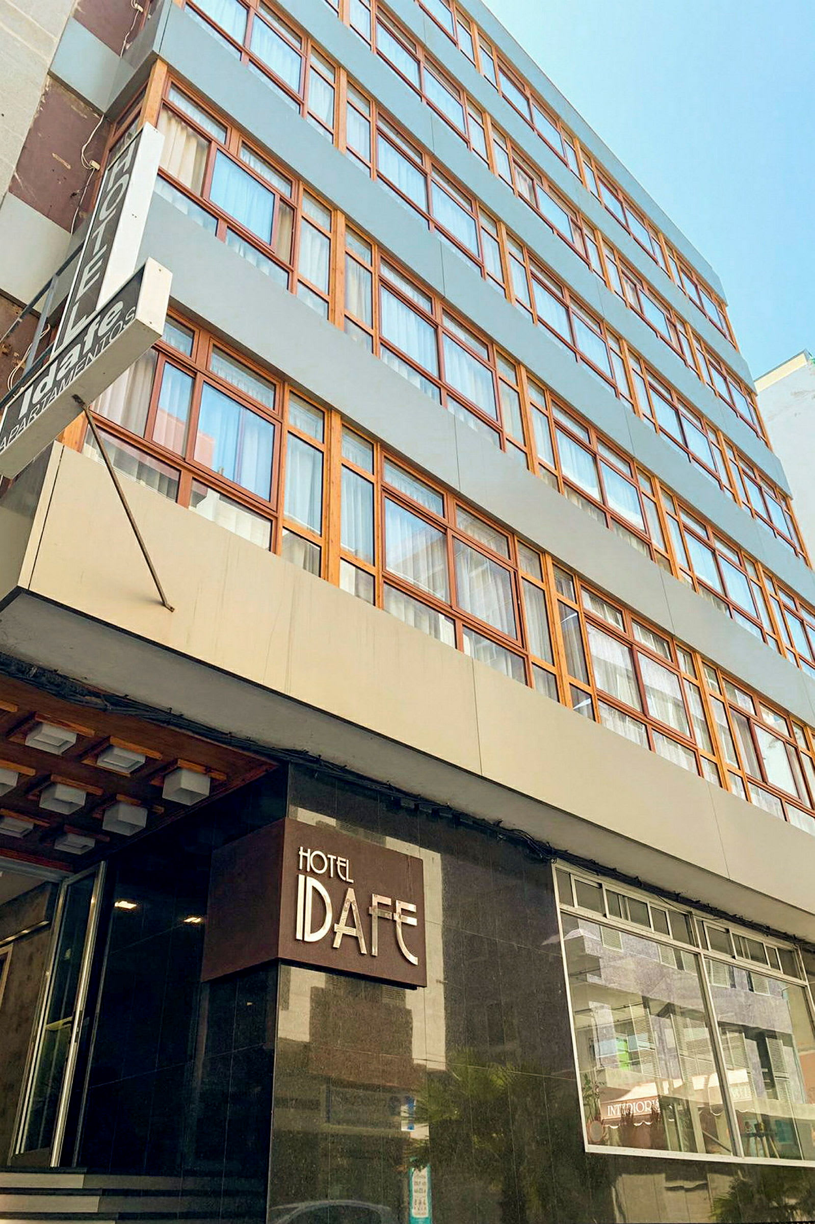 Rakennus, jossa on useita kerroksia, ja sisäänkäynnillä kyltti tekstillä 'Hotel Idafe'. (Tekoälyn luoma teksti)