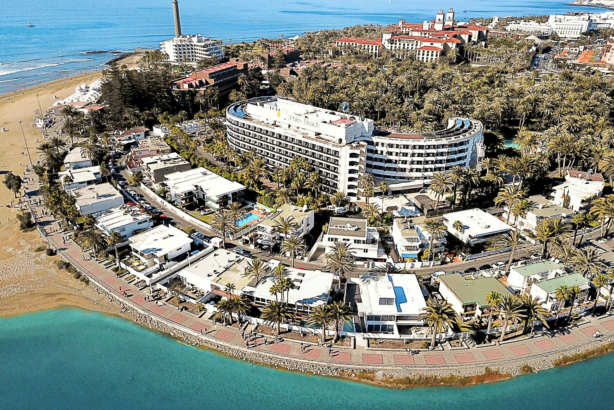Ilmakuva rannikkokaupungista, jossa hotelleja, palmuja ja hiekkaranta. (Tekoälyn luoma teksti)
