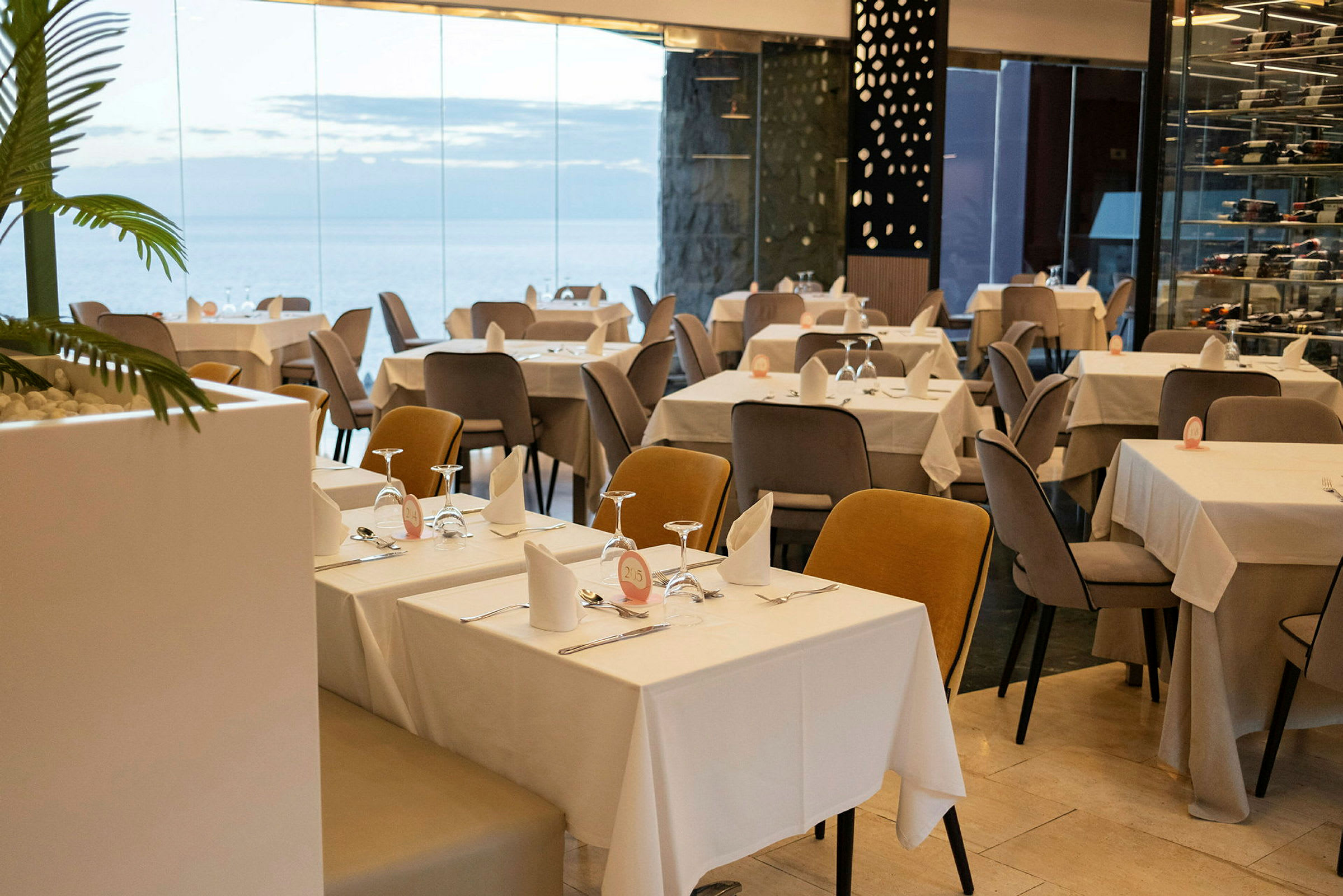 Ravintola, jossa katettuja pöytiä ja tuoleja modernissa ympäristössä lasiseinillä. (Tekoälyn luoma teksti)