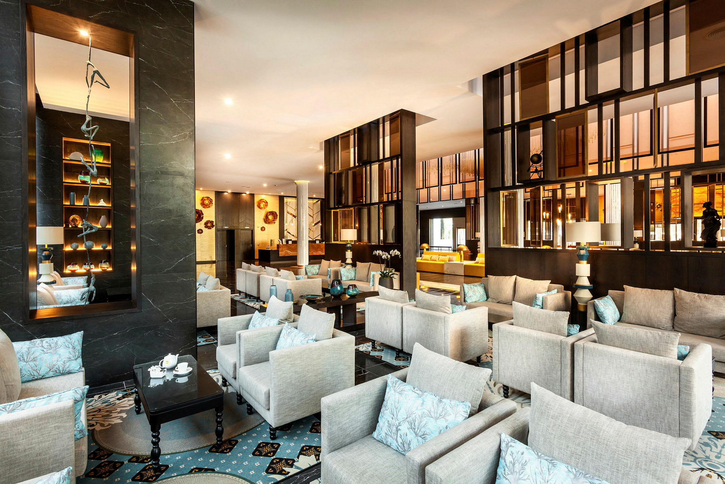 Moderni ja tyylikäs lounge-alue, jossa on harmaita nojatuoleja, sinisiä tyynyjä ja elegantti pöytäkoristelu. (Tekoälyn luoma teksti)