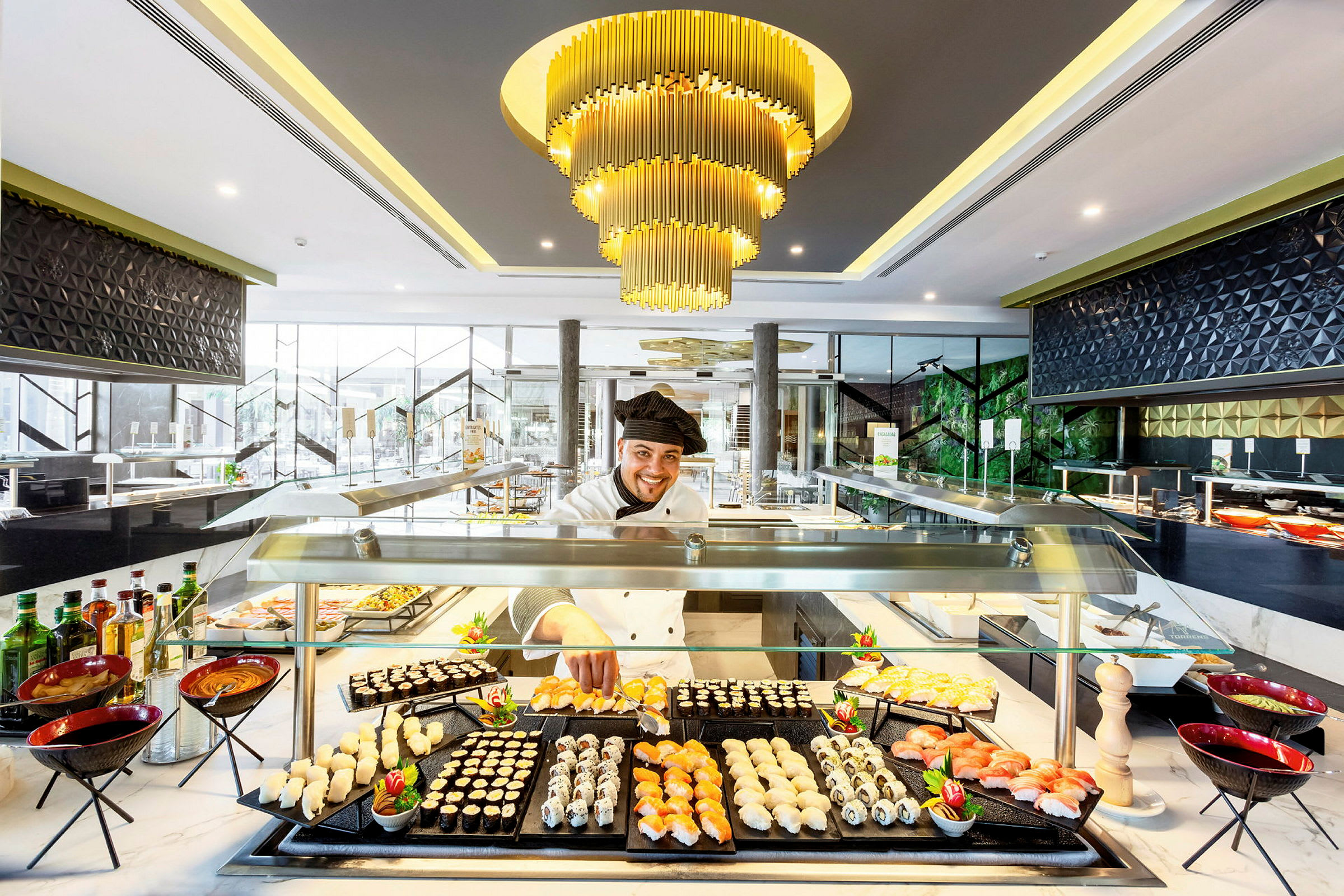 Tyylikäs ruokatarjoilu sushilla ja muilla pikkupurtavilla buffetissa, jota valaisee ylellinen kattokruunu. (Tekoälyn luoma teksti)