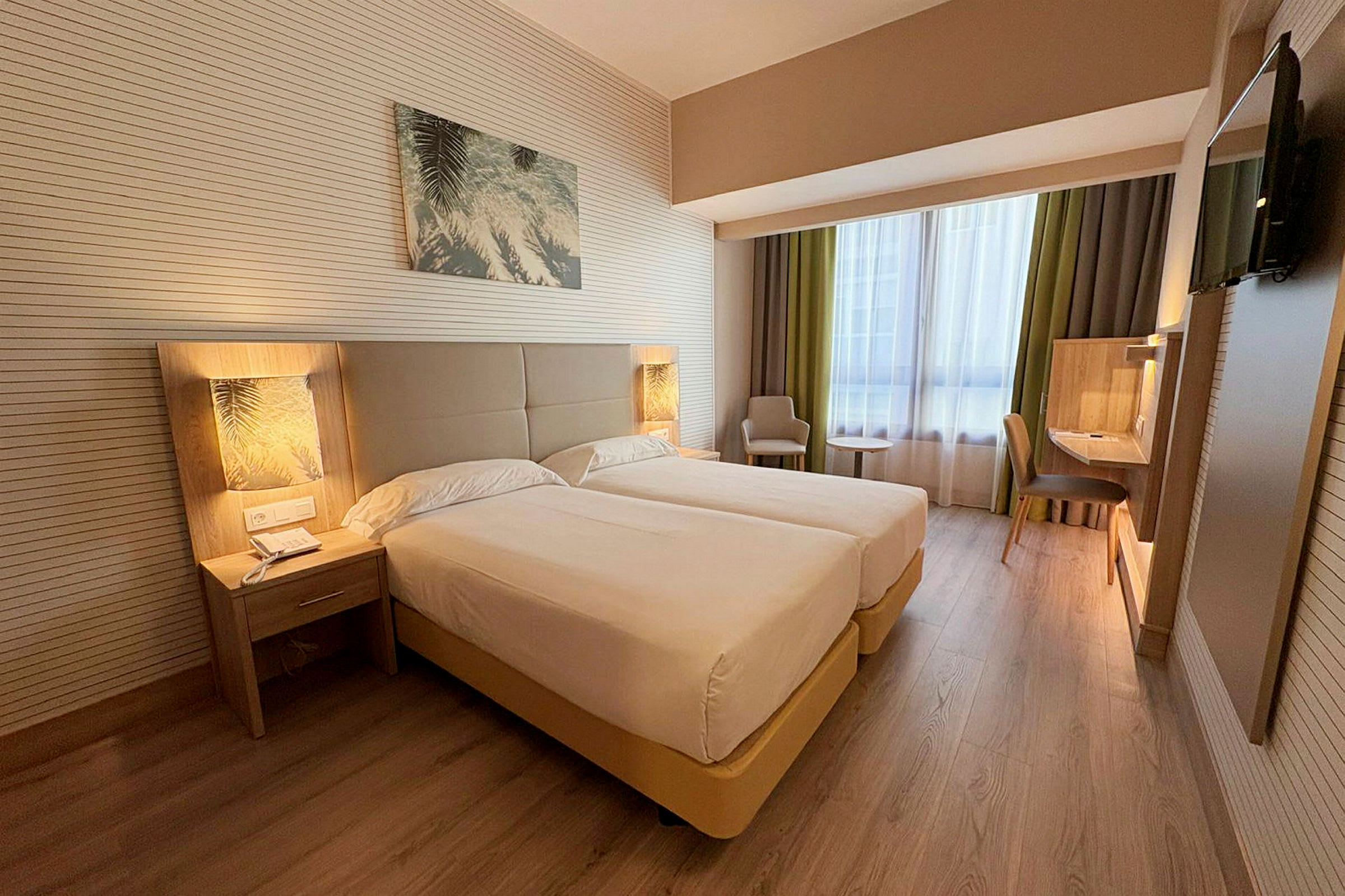 Hotellihuone, jossa on kaksi yhden hengen vuodetta, yöpöytä, työtila ja nojatuoli ikkunan vieressä. (Tekoälyn luoma teksti)