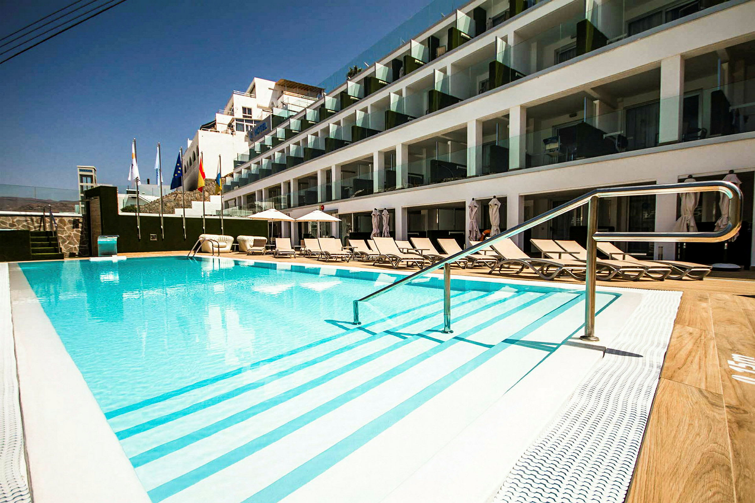 Ulkouima-allas hotellilla, jossa on aurinkotuoleja ja lasiparvekkeita. (Tekoälyn luoma teksti)